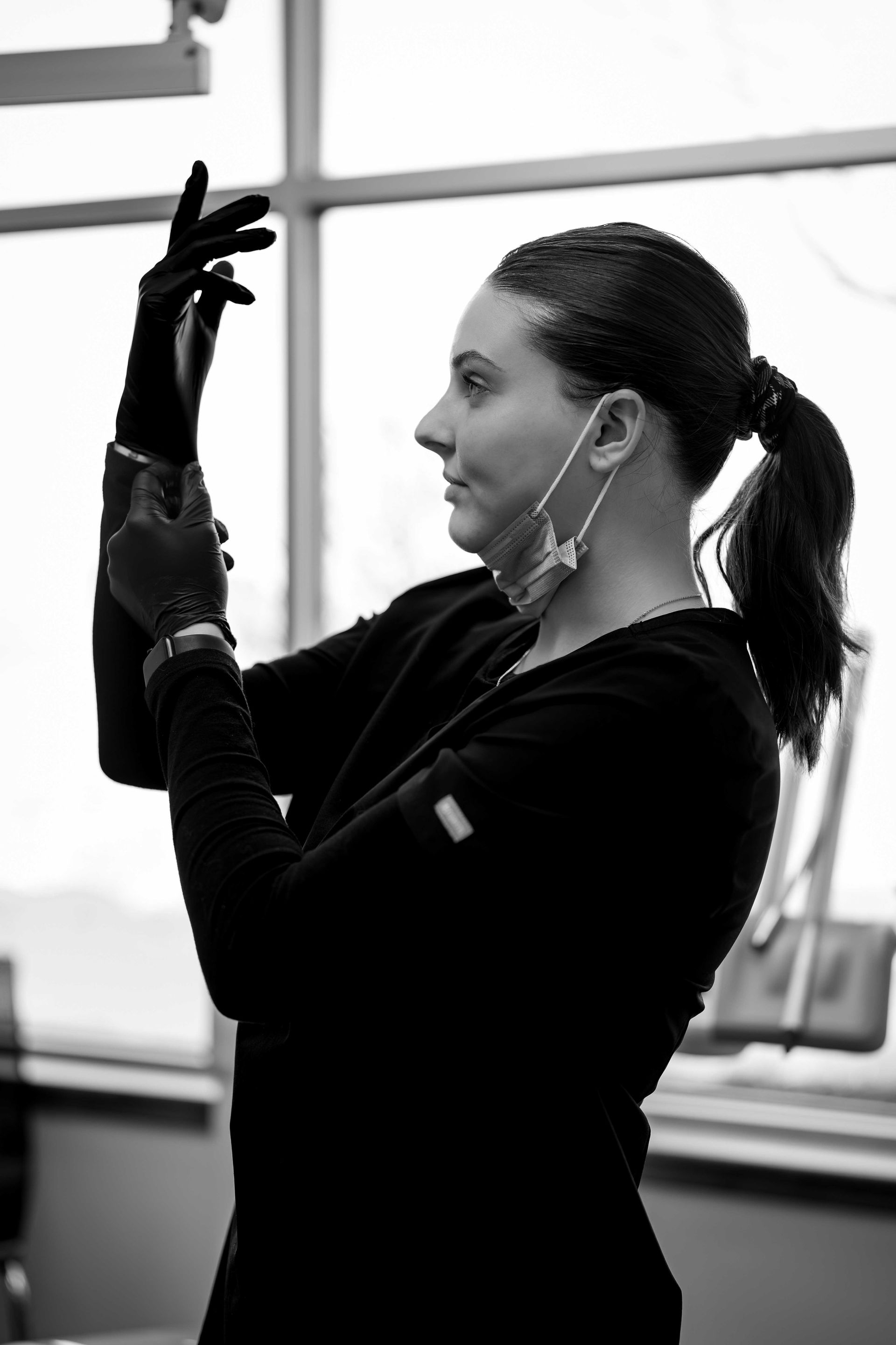 Person in black gloves adjusting a device, in profile near a window.