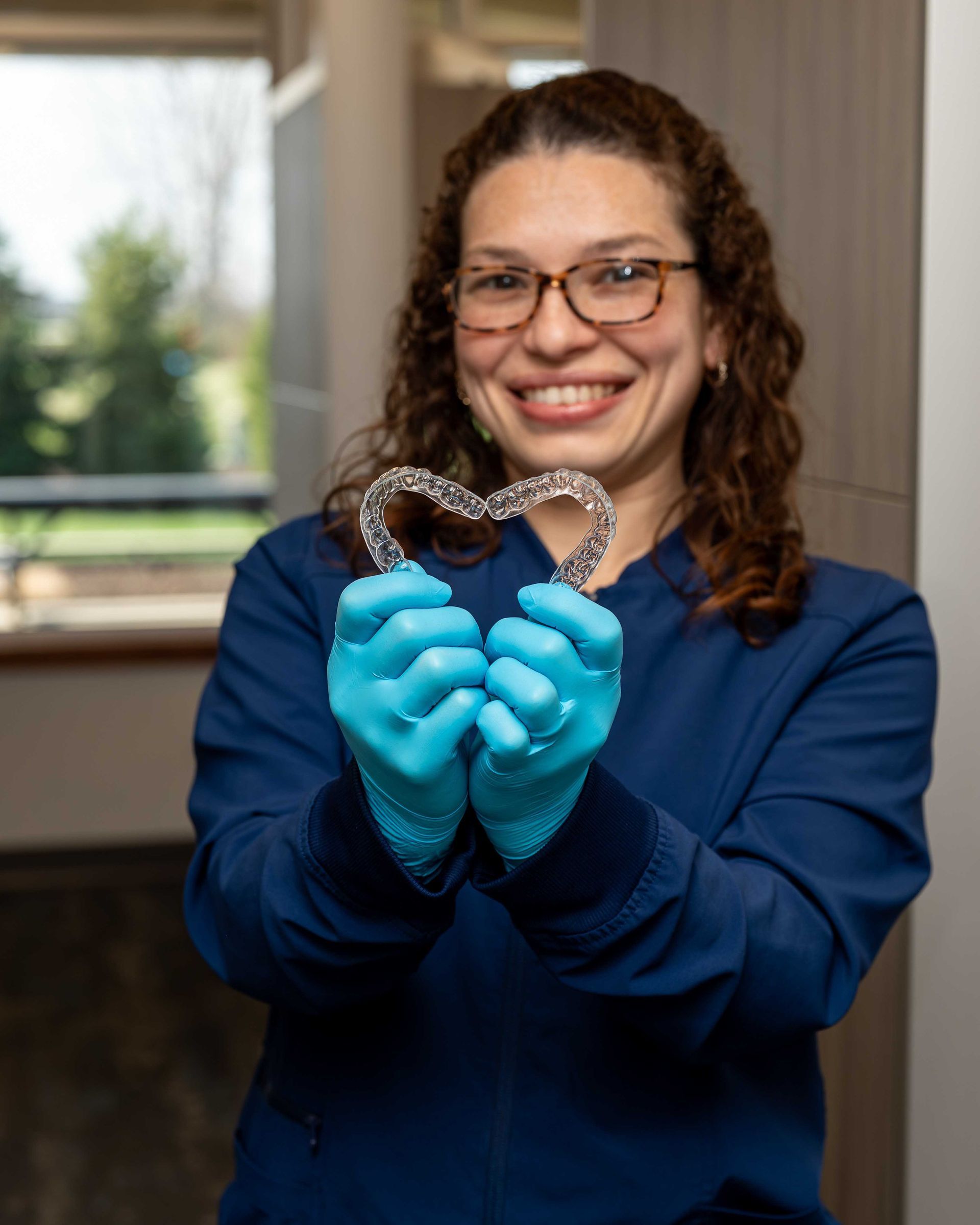 Woman in blue gloves holding a heart-shaped wire sculpture and smiling indoors