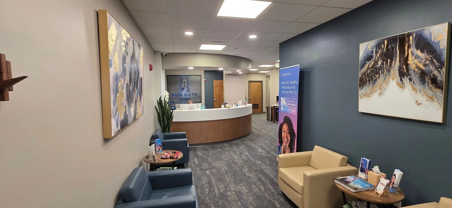 Modern clinic waiting room with blue and tan chairs, a reception desk, and wall art