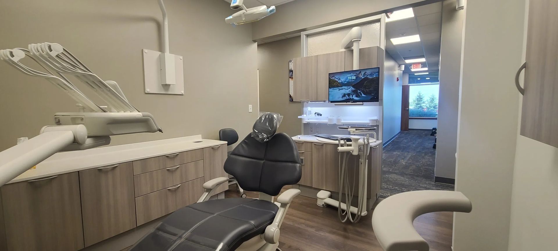 Dental exam room with black chair, cabinets, monitor, and overhead light