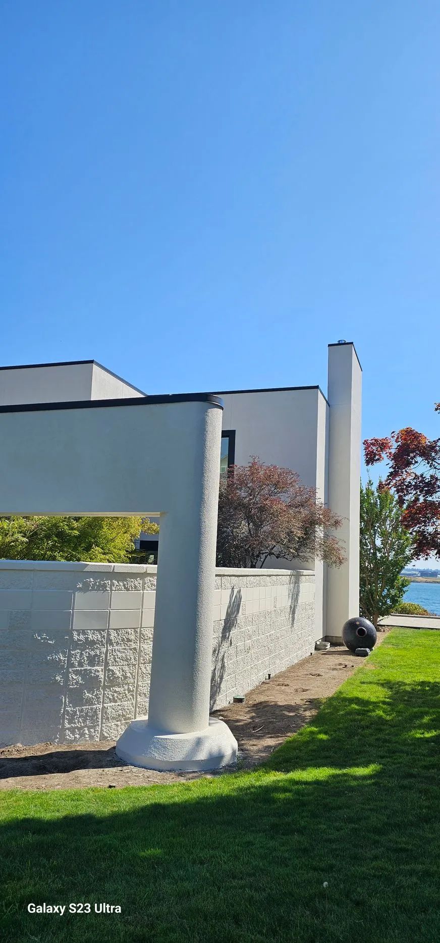 White pergola posts and beam beside a wall in a sunny yard with green grass and blue sky