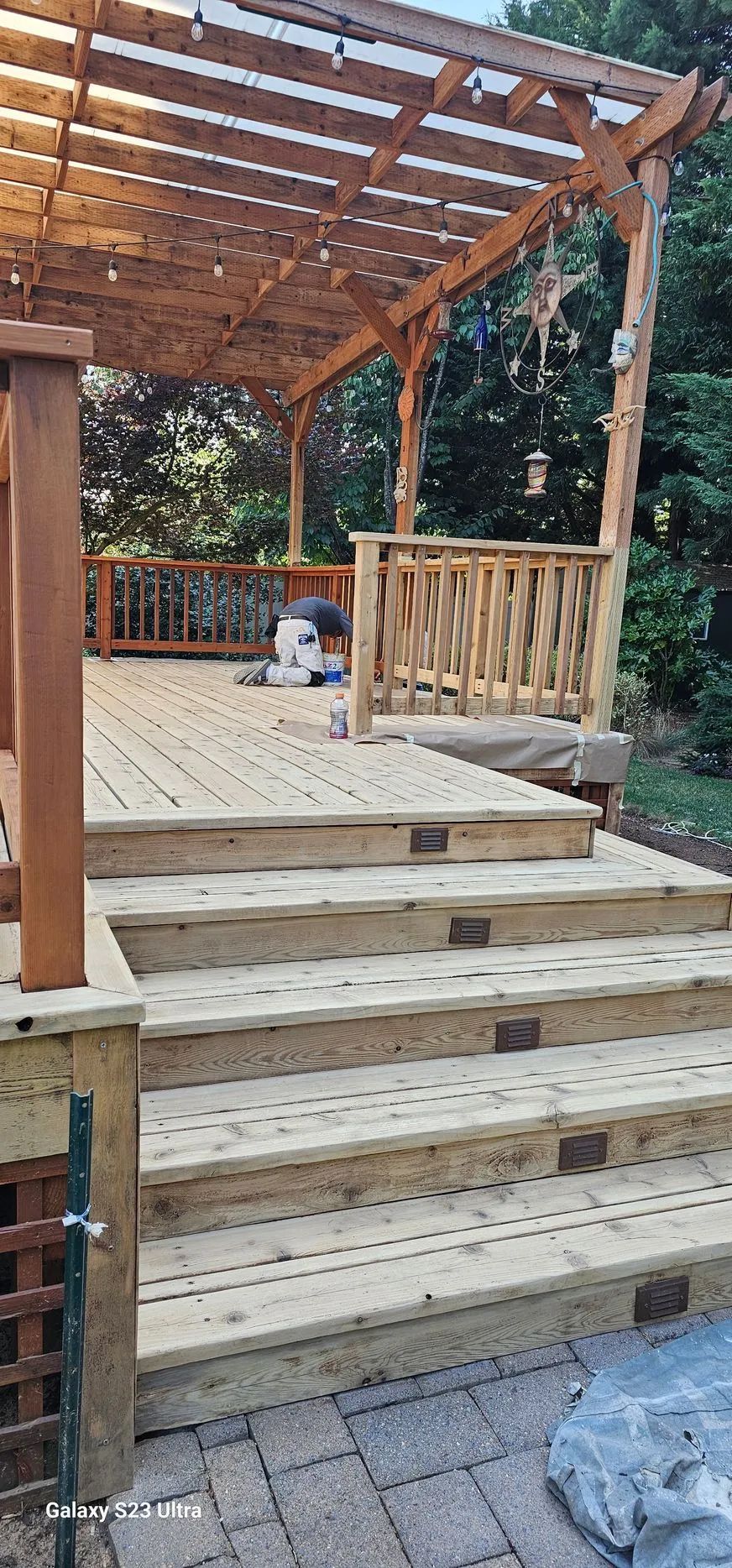 Wooden backyard deck stairs leading to a pergola-covered patio with railings and potted plants