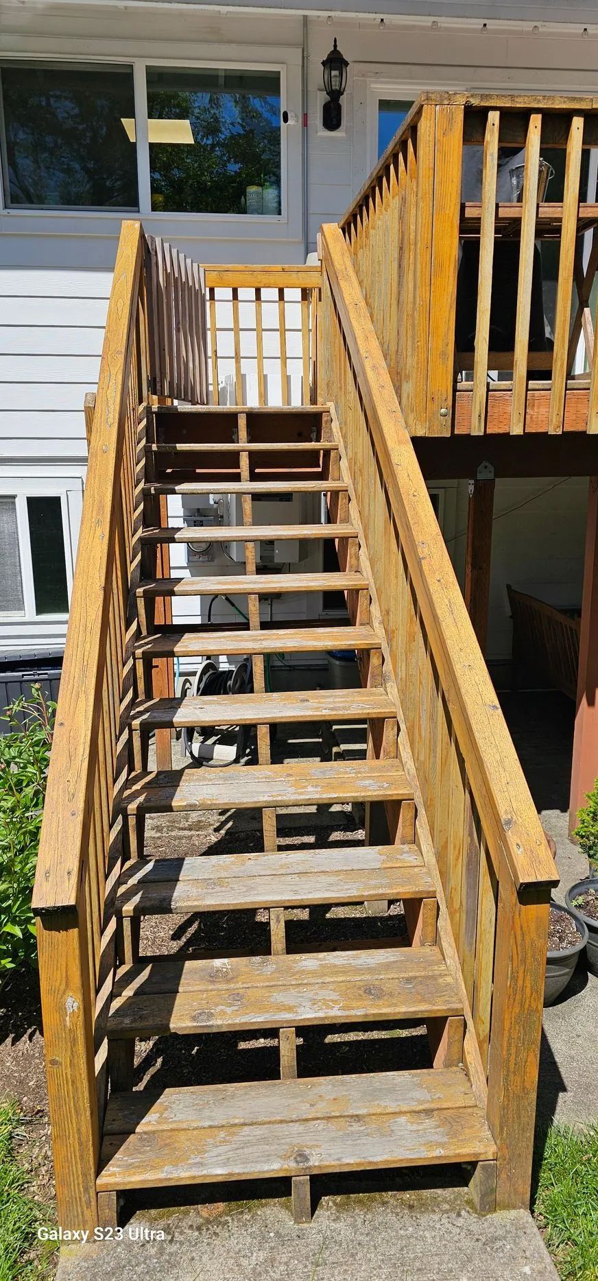 Wooden outdoor stairs leading to a porch, with railings and a house window in the background