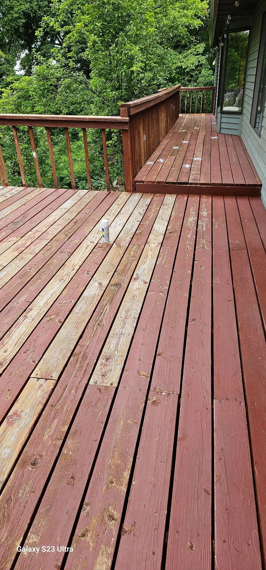 Red wooden deck with railing beside trees and greenery