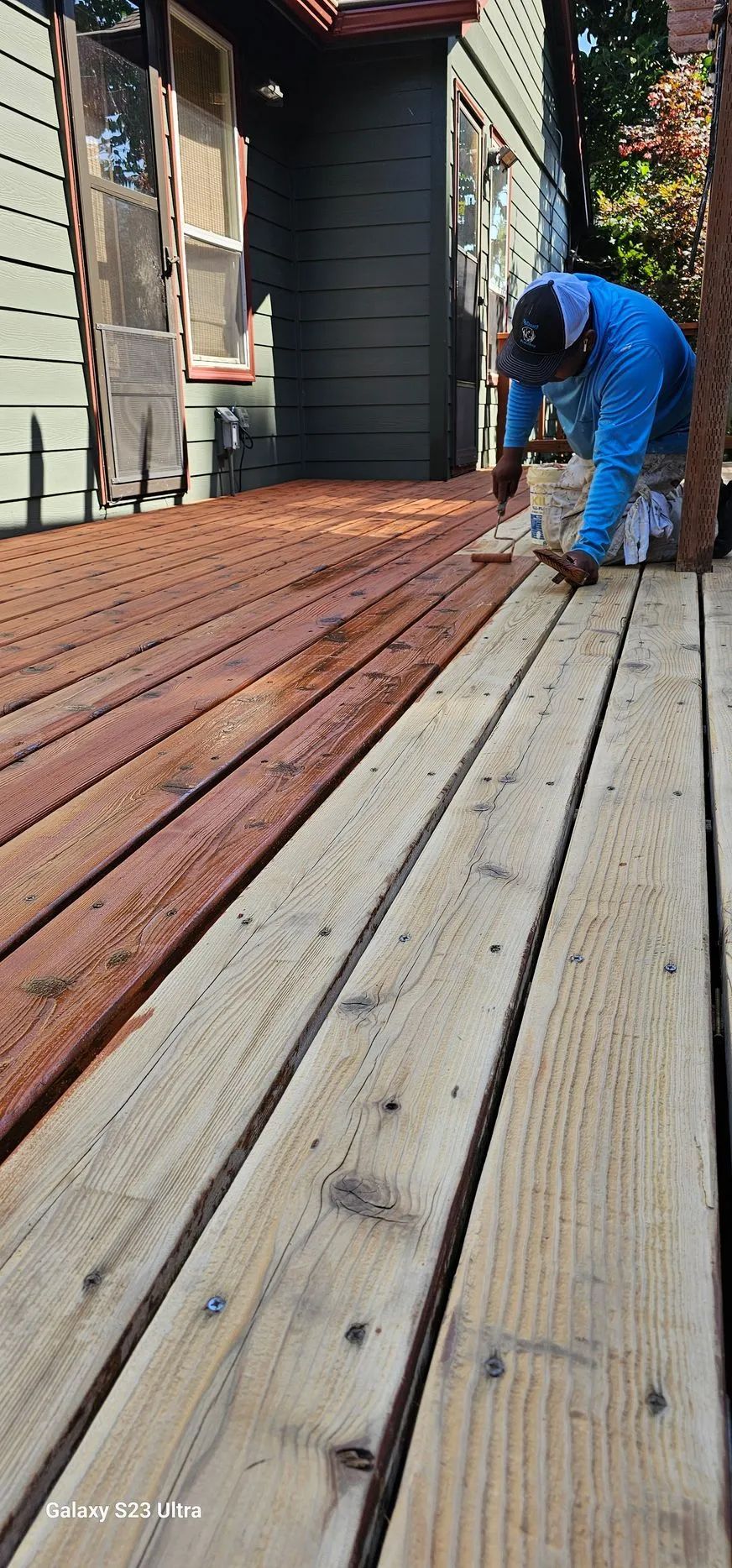 Worker in blue overalls measuring wooden deck boards beside a house.