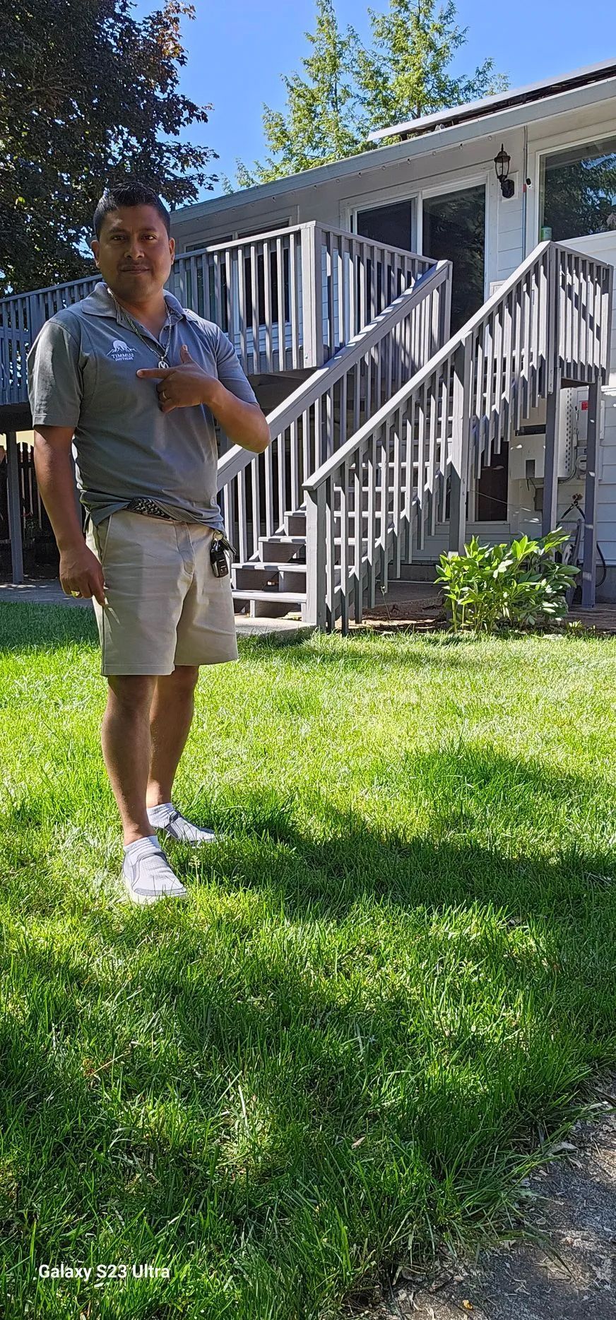 Person standing on a grassy lawn in front of a white house with a staircase and porch.