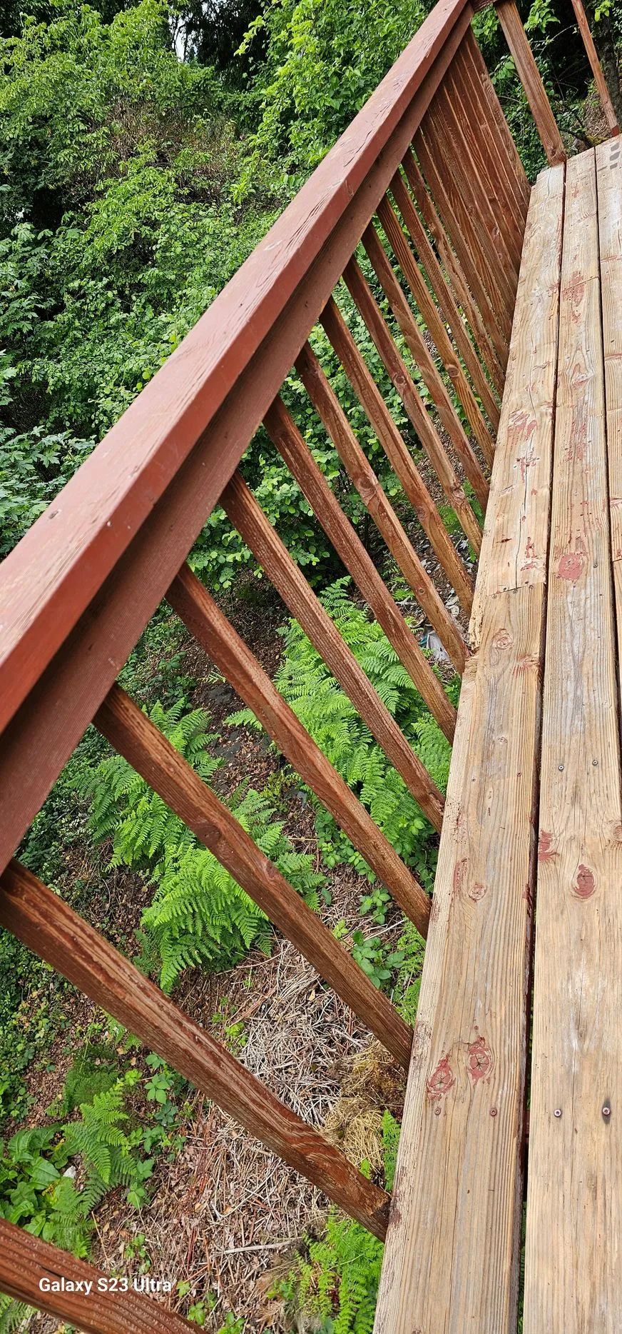 Weathered wooden railing beside a narrow deck, with green forest and rocky slope below