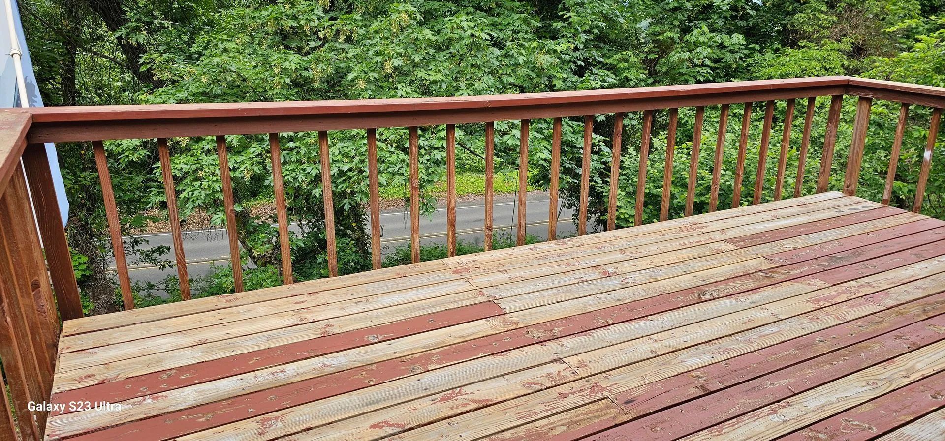 Wooden deck with railing overlooking lush green trees and a stream below