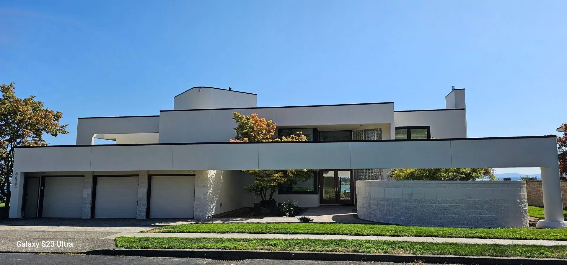 Modern white house with a flat roof, large windows, and a low stone wall under a clear blue sky