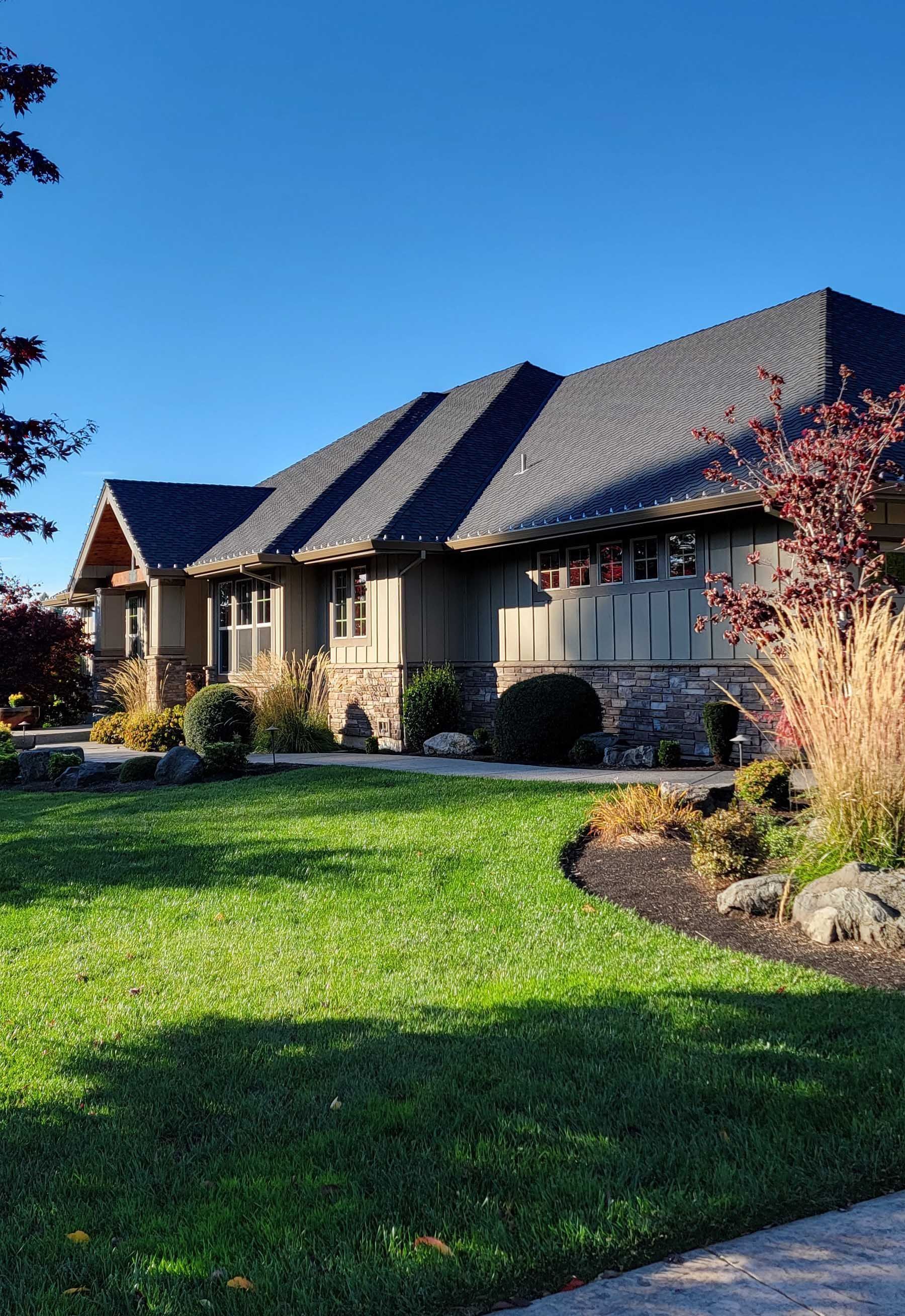 Suburban house with stone facade, dark roof, and a green lawn under a clear blue sky