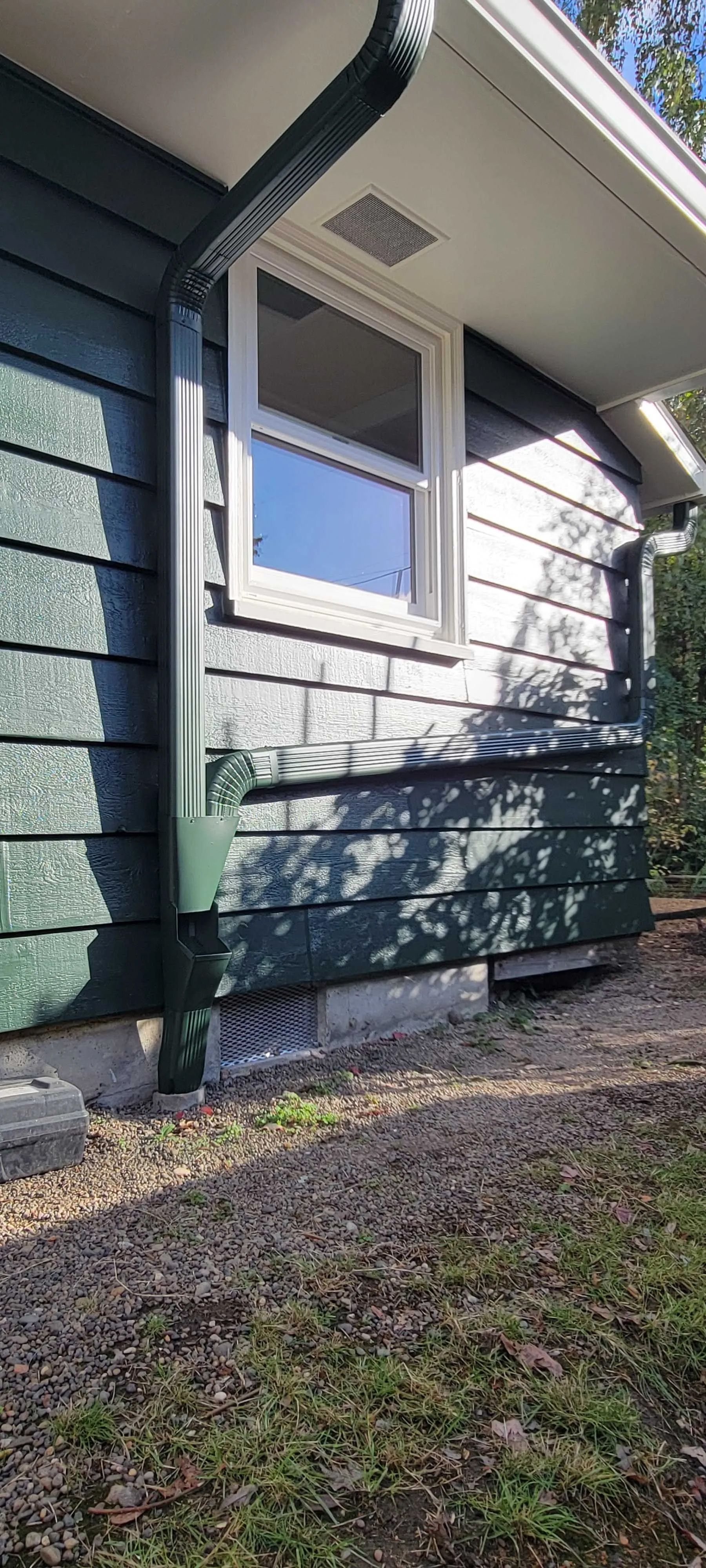 Side view of a house exterior with white siding, a window, and green support posts over a gravel and grass yard