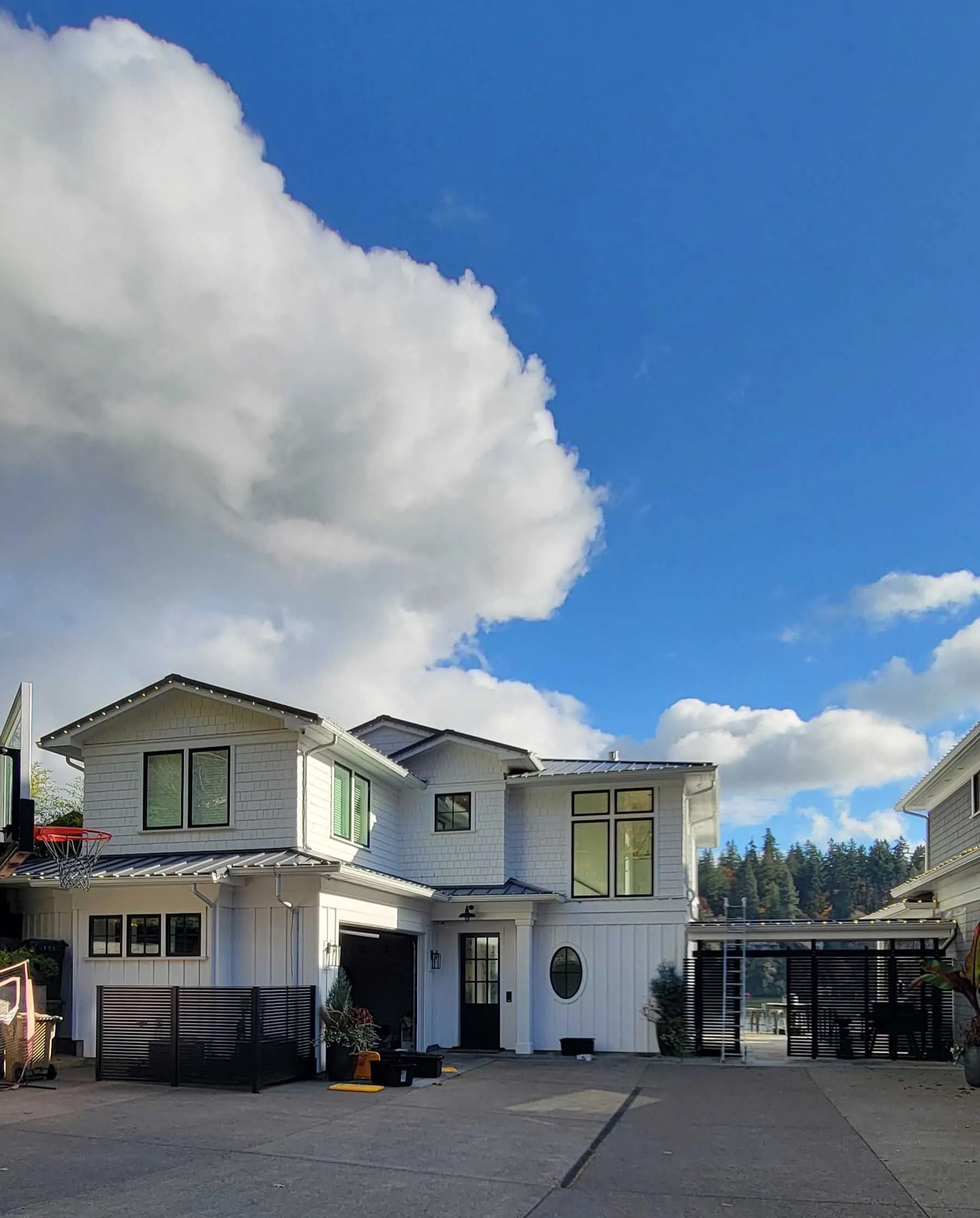Two-story white house with black gate and driveway under a partly cloudy blue sky