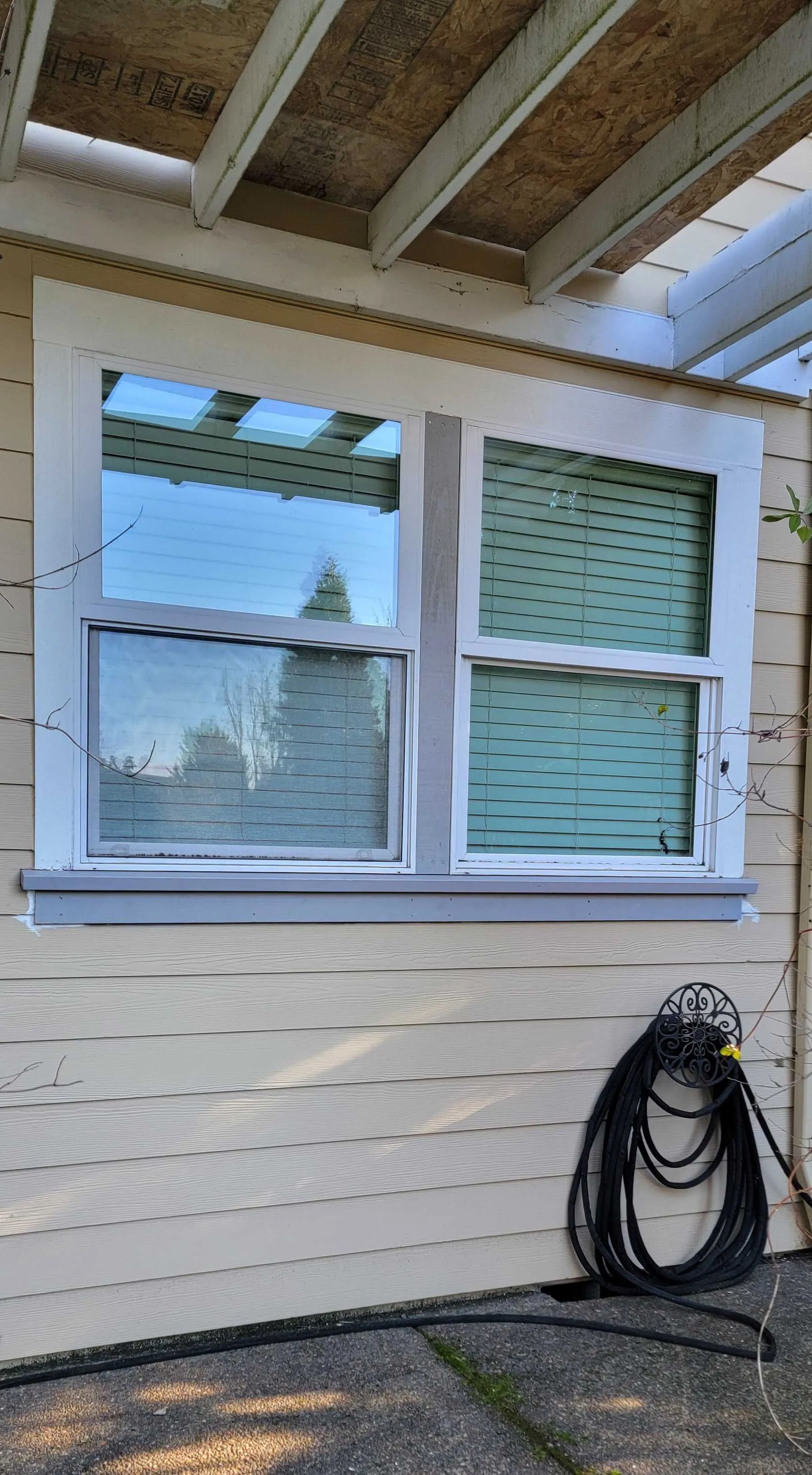 House exterior with two white-framed windows, beige siding, and a coiled black hose on the wall