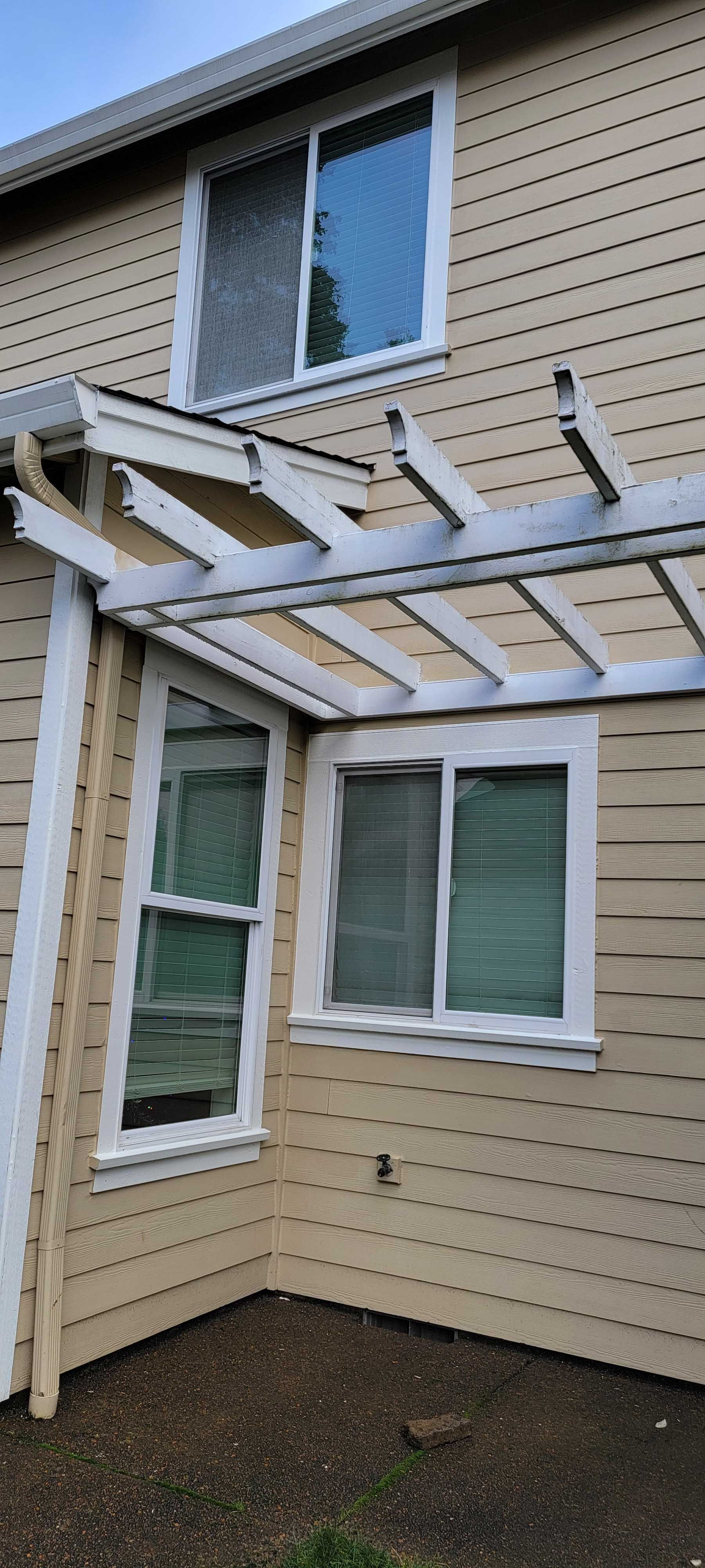 White pergola over a beige house patio with windows and a dirt yard beneath
