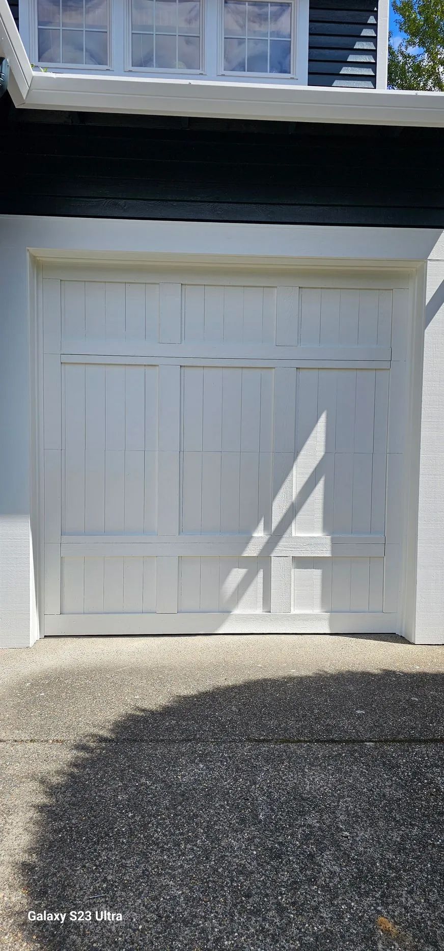 White garage door with decorative panels beneath a dark overhang and blue siding above