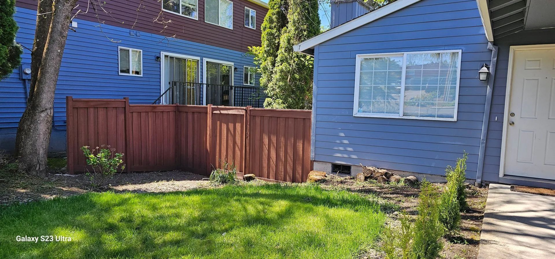 Blue house exterior with fenced backyard, green lawn, and a side walkway