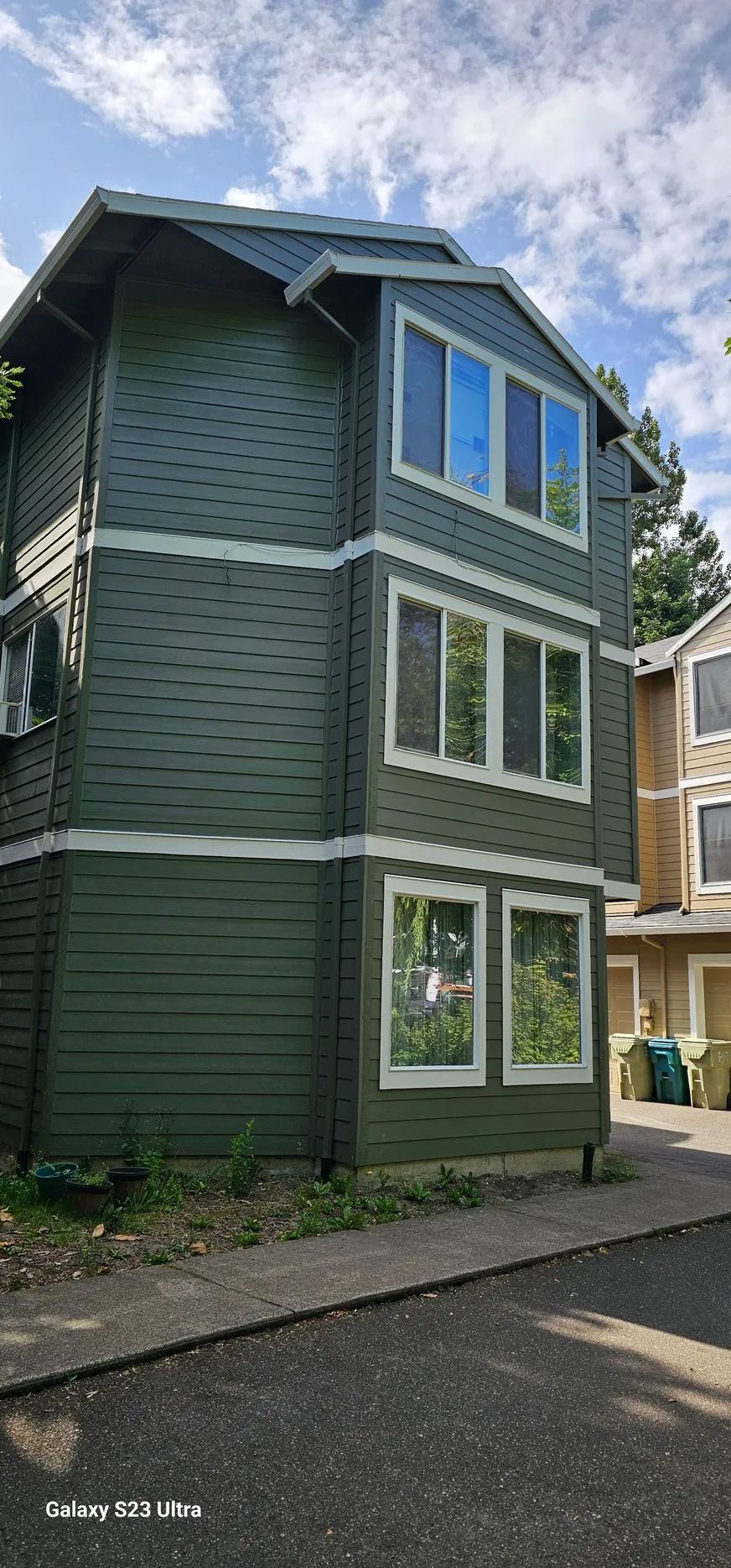 Tall green townhouse with white trim and blue windows beside a paved driveway