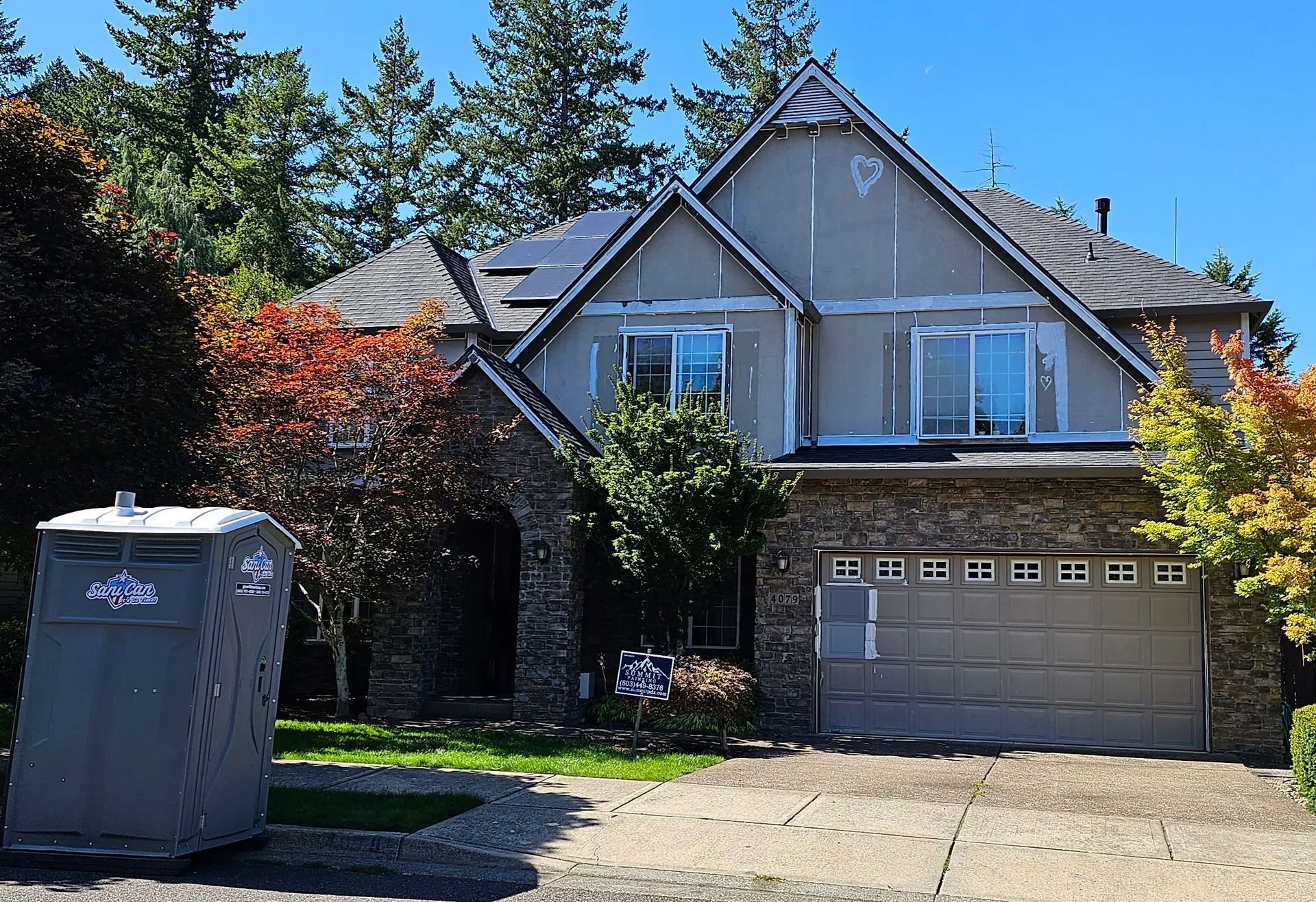 Suburban house with a garage, trees, and a portable toilet in the driveway