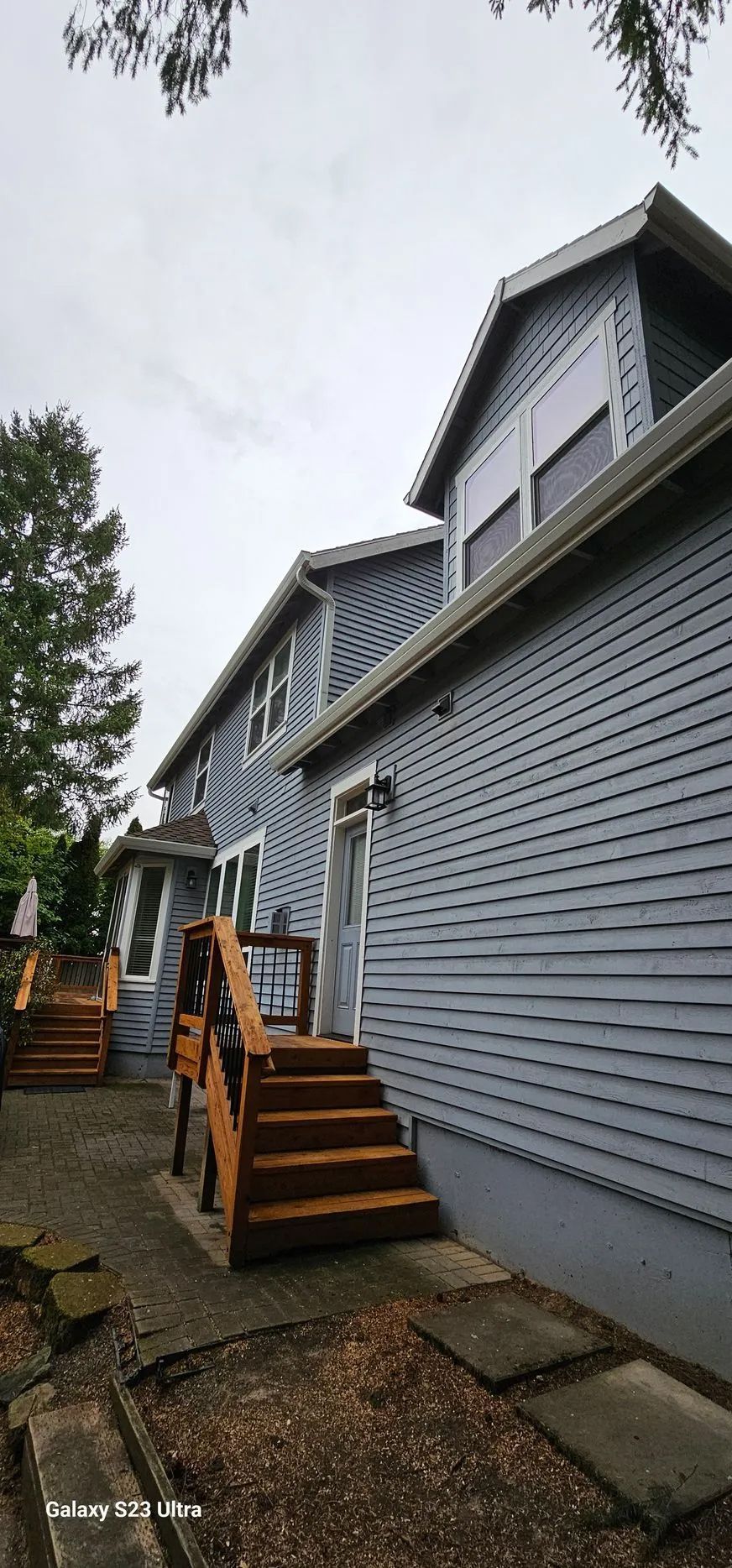 Exterior of a gray house with multiple wooden stairways along a gravel walkway, viewed from below