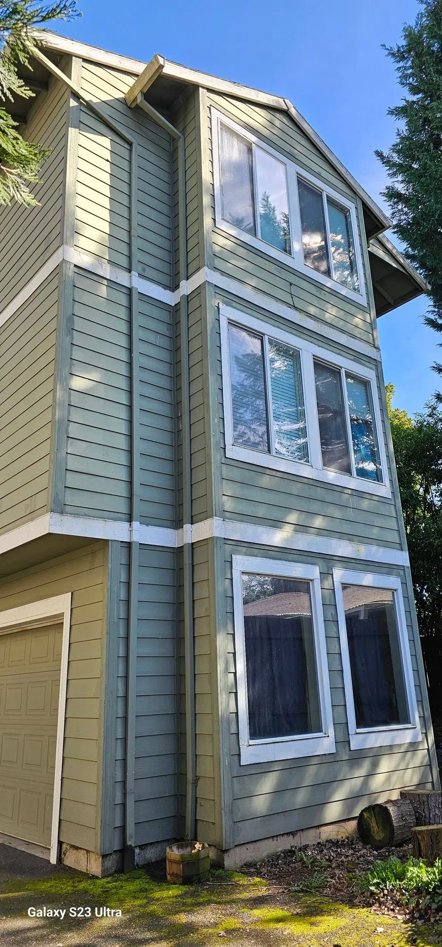 Three-story pale green house with white trim and large front windows under a blue sky