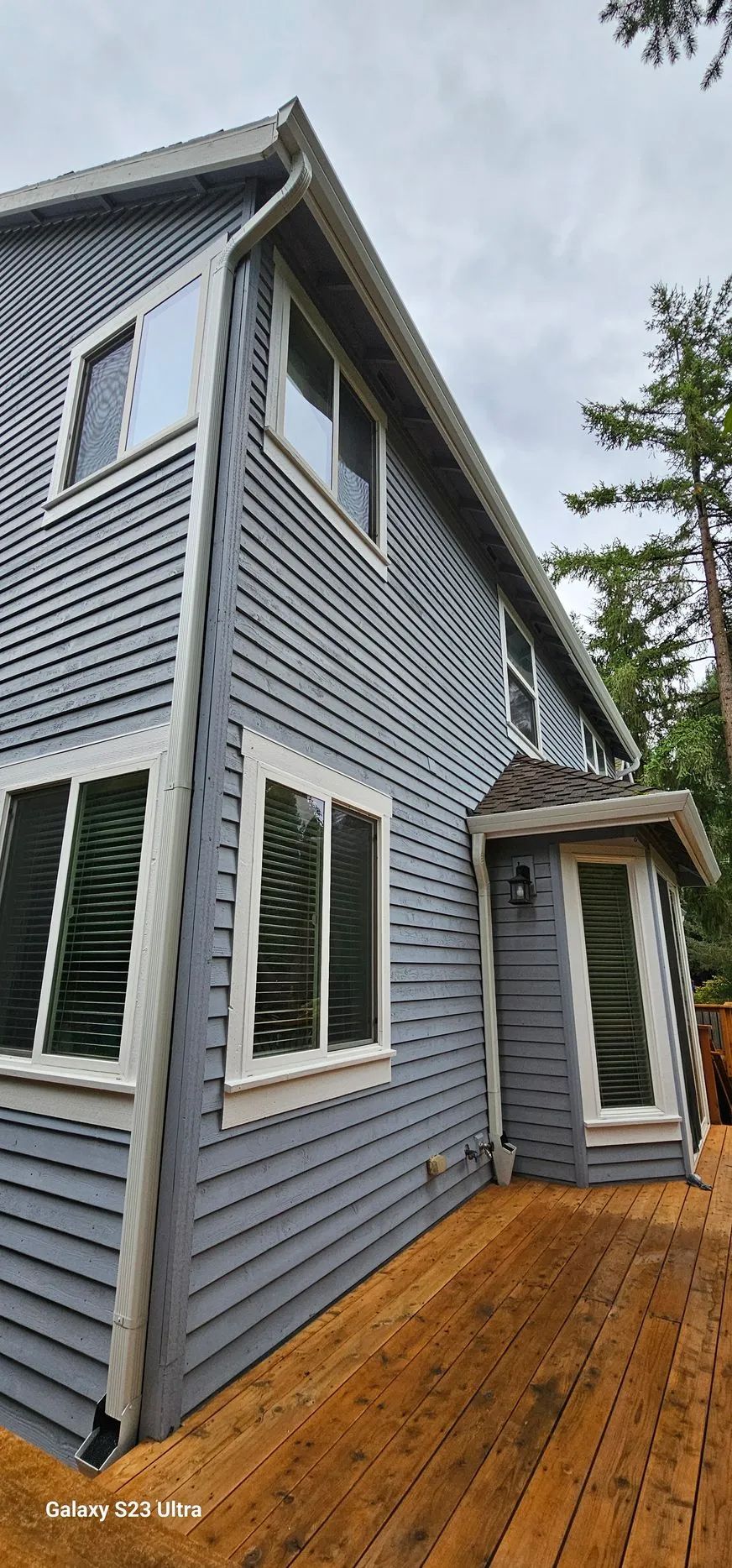 Blue-gray house exterior with white trim and a wooden deck under an overcast sky