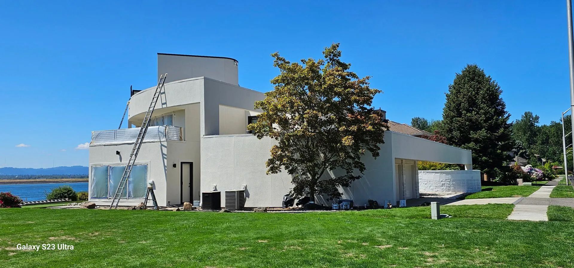 Modern white building with a curved facade beside a grassy lawn and trees under a clear blue sky.