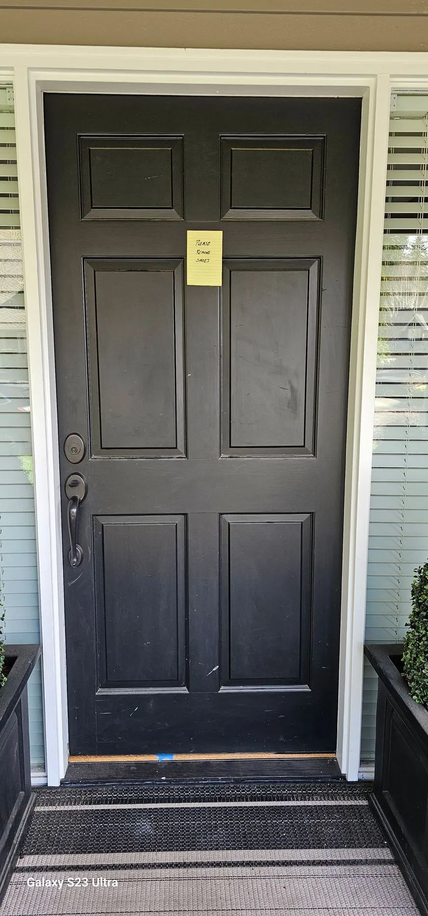 Black paneled front door with a yellow notice, framed by white trim and sidelights.