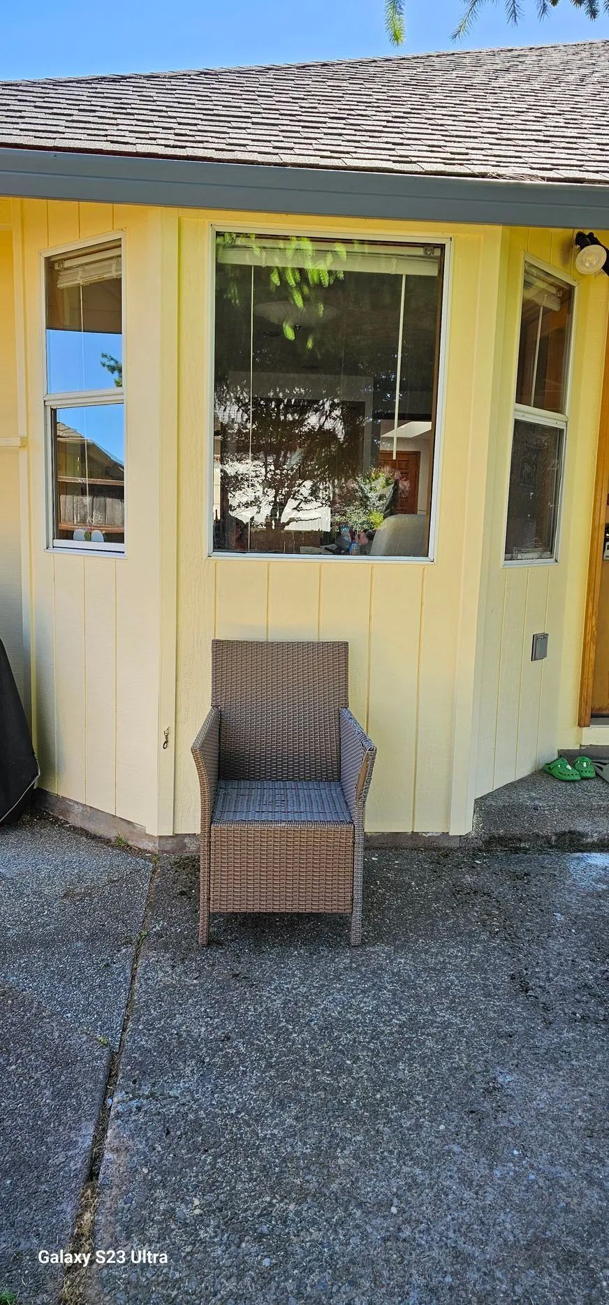 Yellow garden shed with windows and a wicker chair on a gravel path