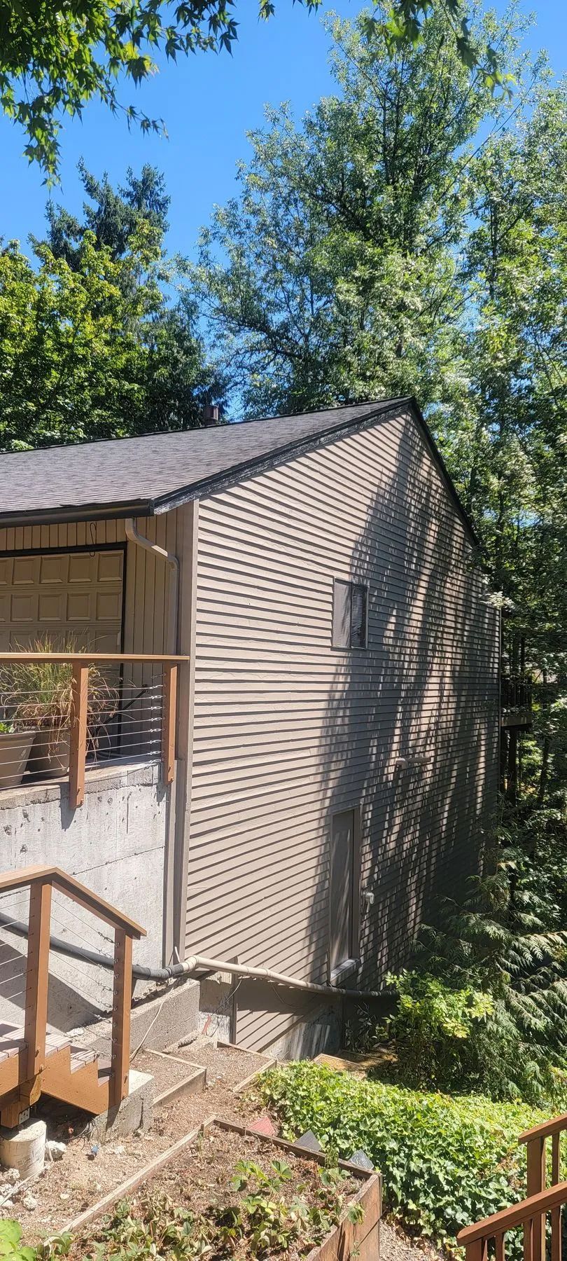 Wooden cabin exterior with stairs, surrounded by trees and greenery under a blue sky
