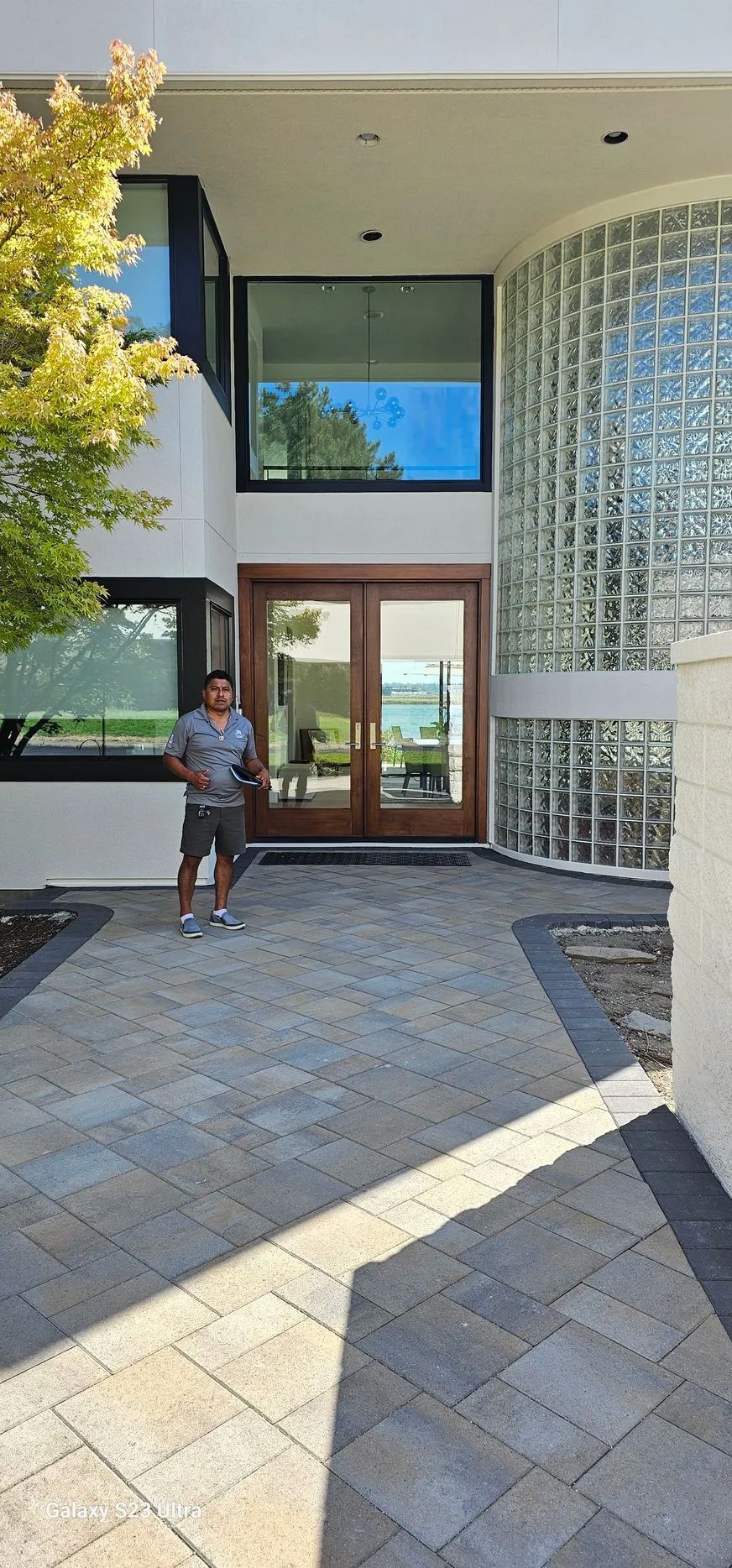 Person standing at the entrance of a modern building with glass doors and curved glass block wall.