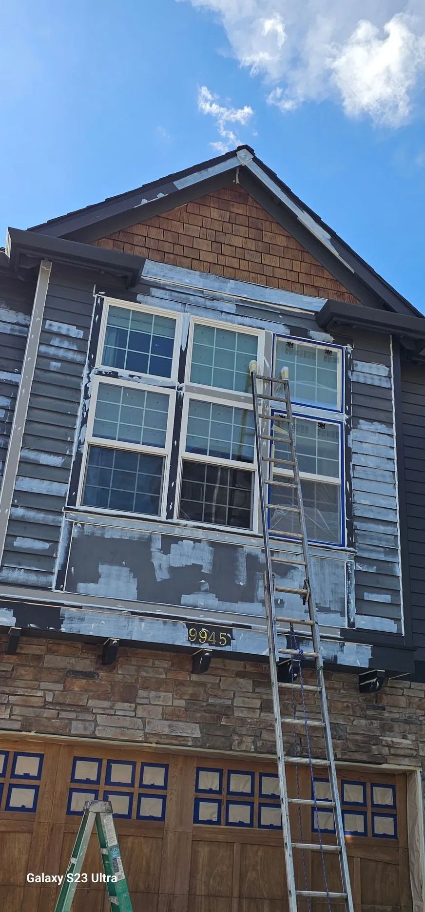 Weathered townhouse facade with peeling gray paint, white-trimmed windows, and a brick gable above a brown garage door