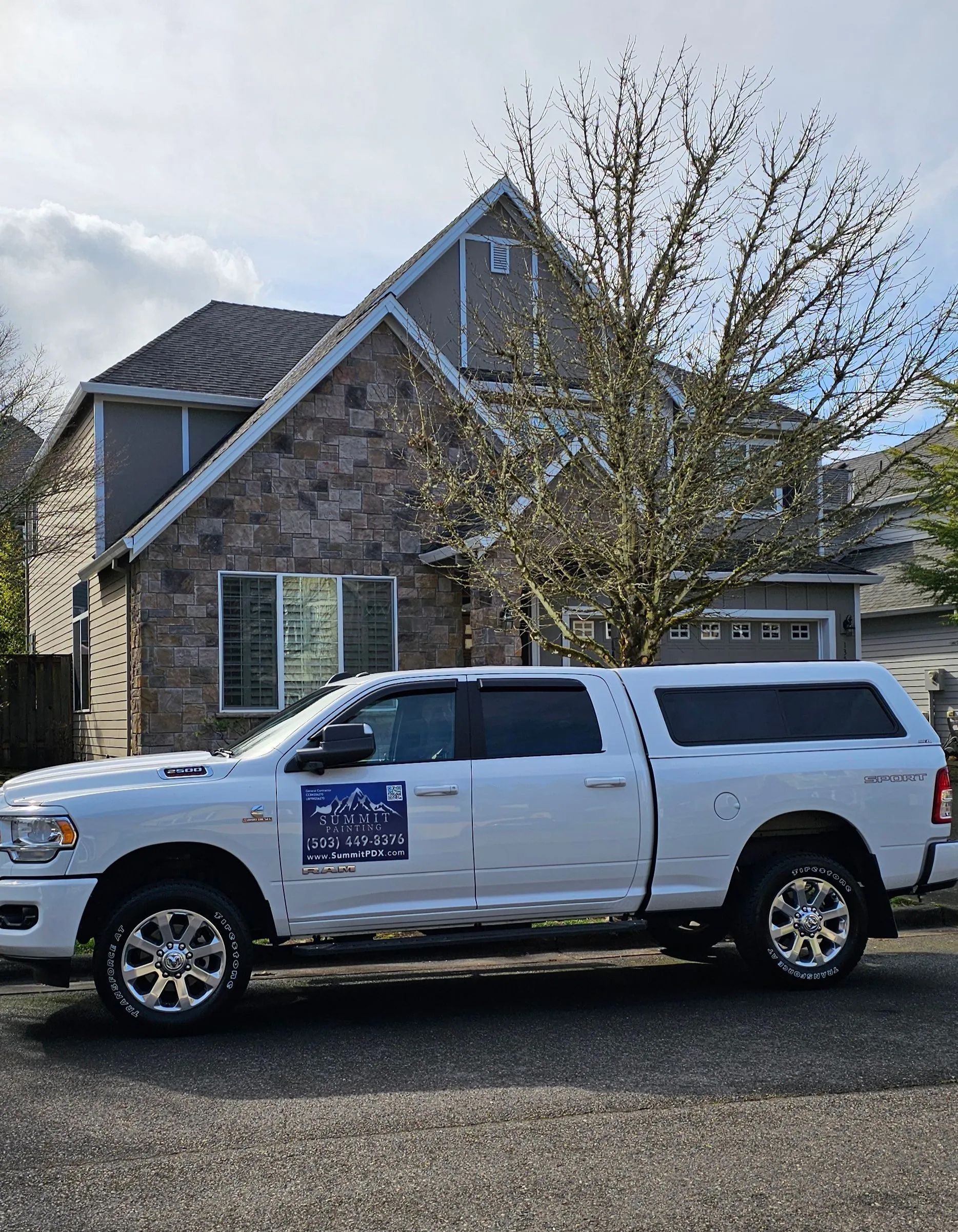 White pickup truck parked in front of a stone house with a tree and garage in the background