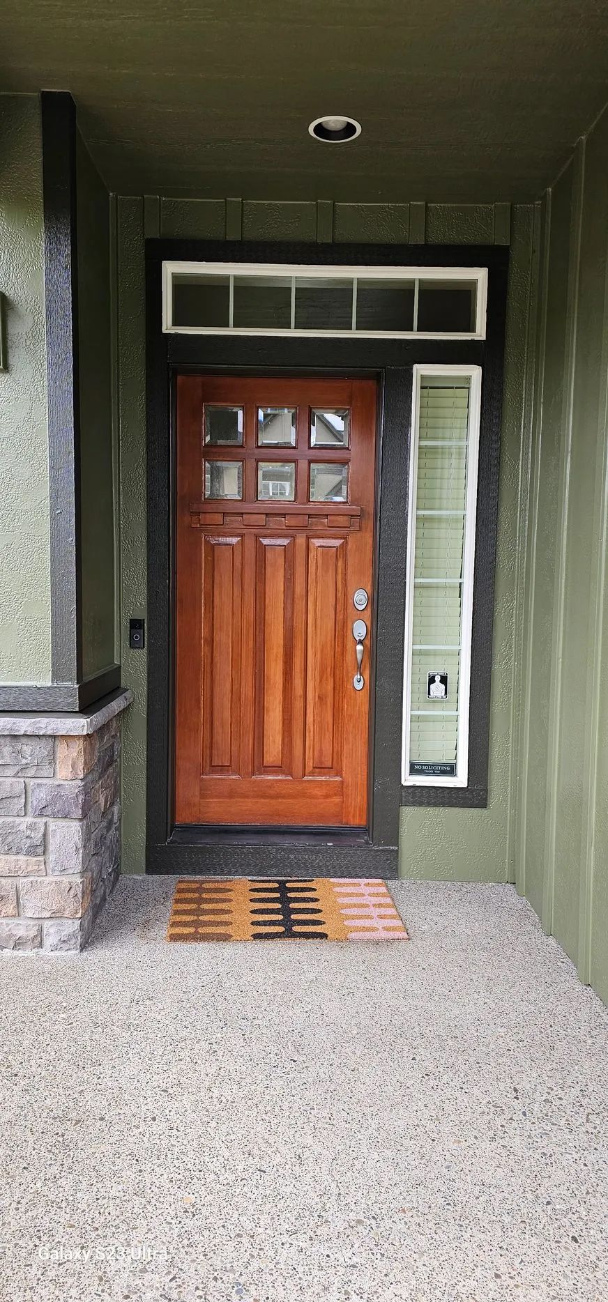 Front entry with a wooden door, green siding, transom window, and stone porch columns