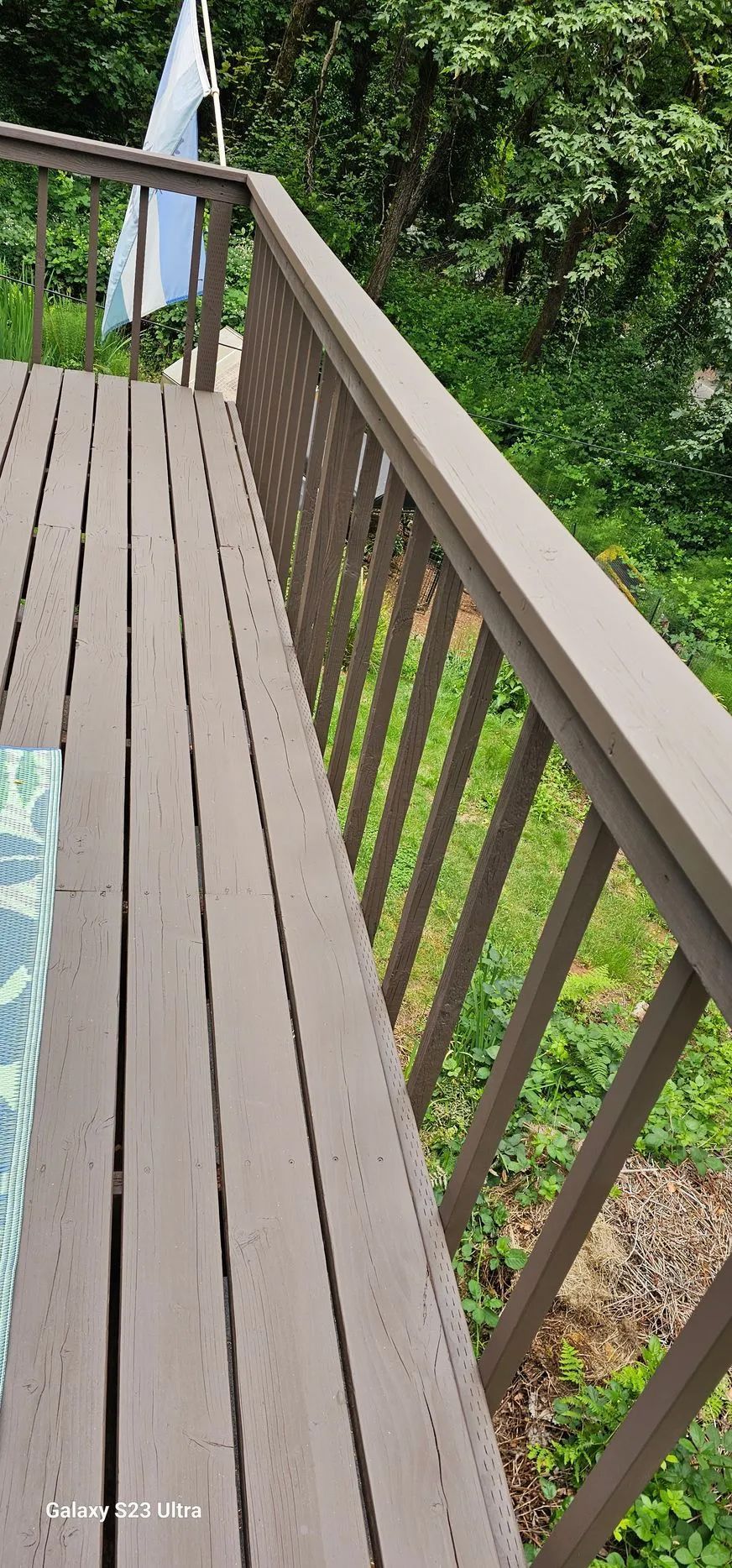 Wooden deck with brown railing overlooking lush green trees and a garden below