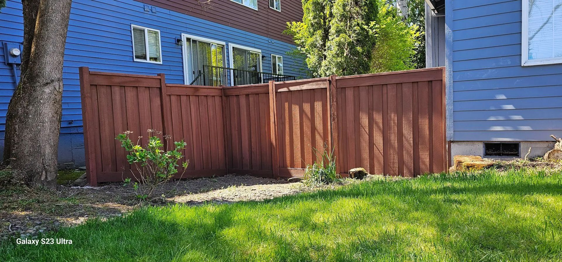 Blue house with a wooden fence and green lawn in a sunny yard