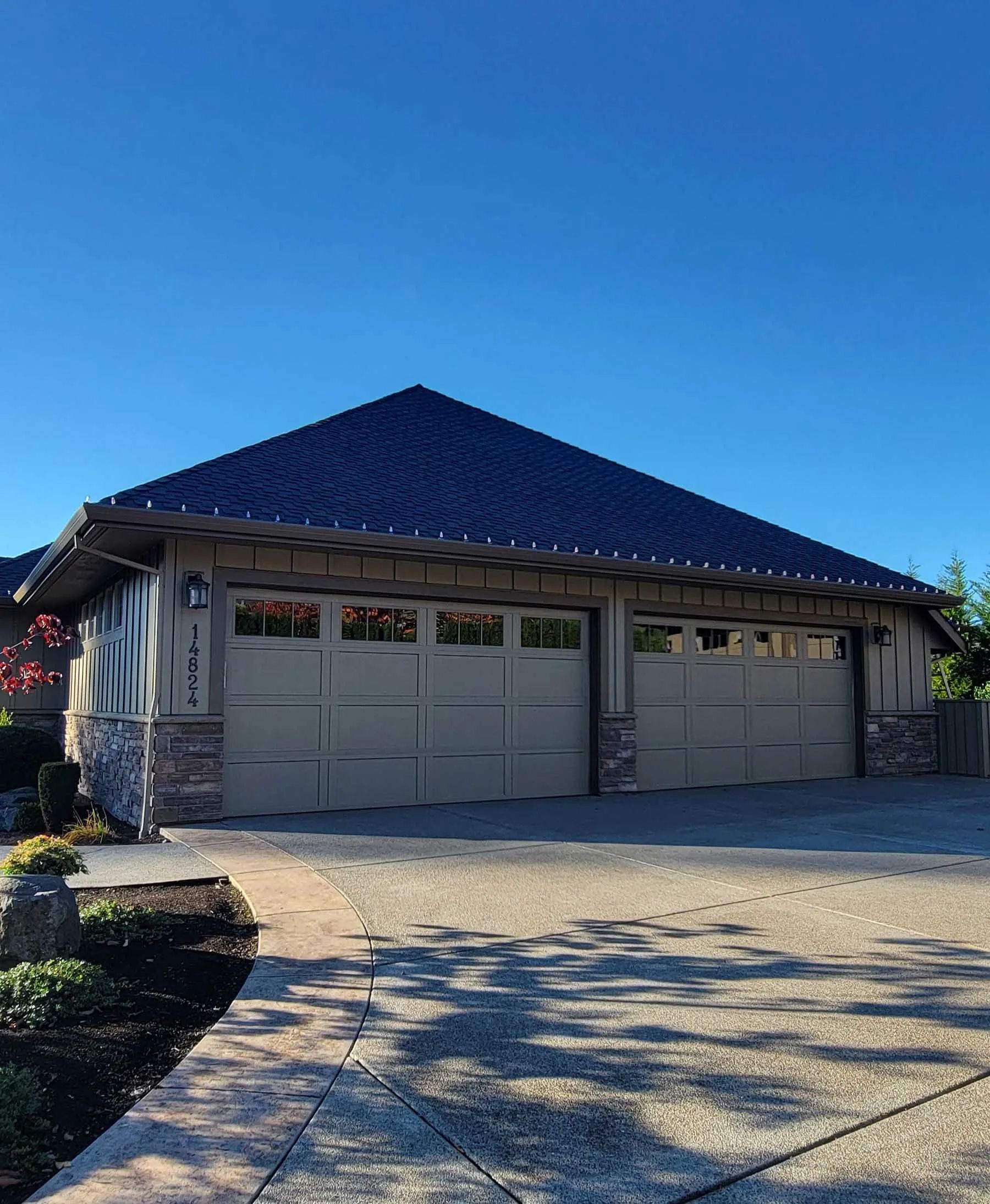 Single-story house with a dark blue roof, beige garage doors, and a sunny driveway under a clear sky
