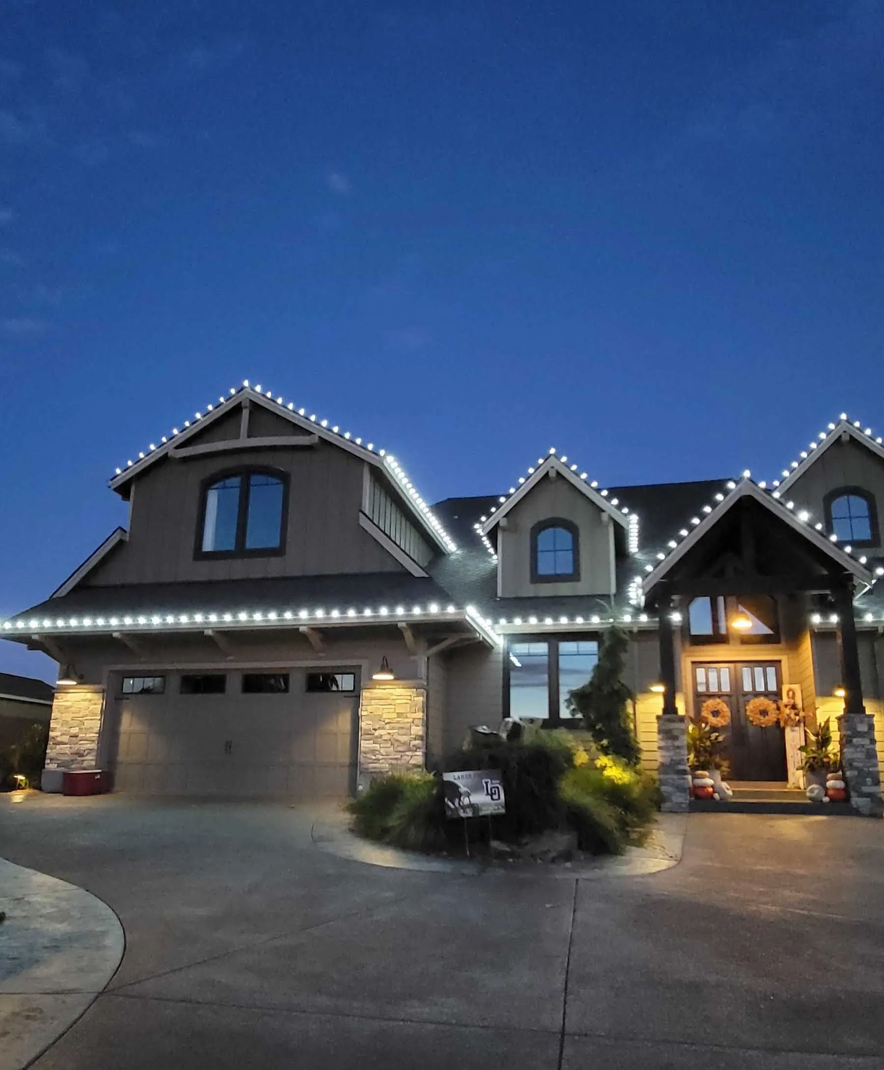Suburban house at dusk with lit roofline, stone garage, and warmly lit front entry.