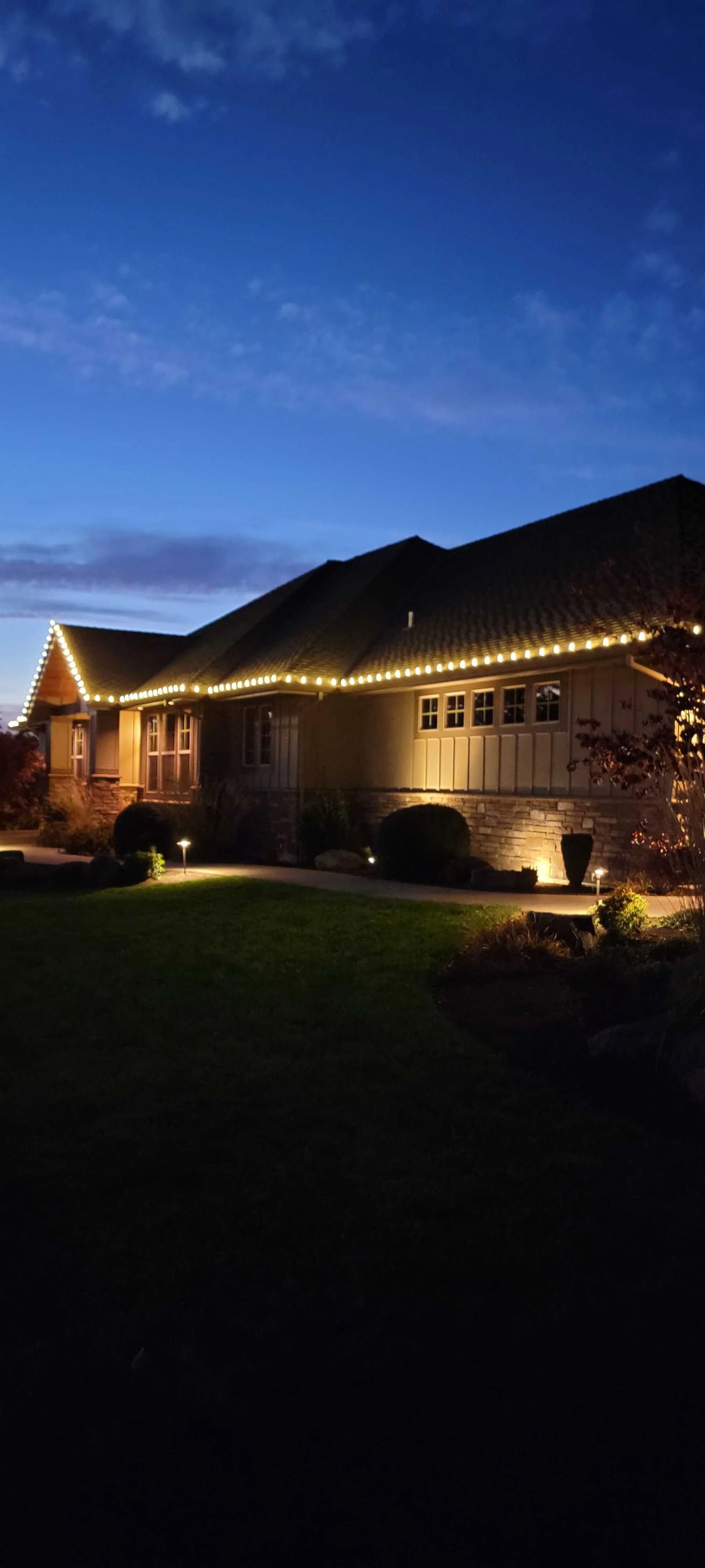 House exterior lit by warm string lights at dusk with a dark blue sky overhead