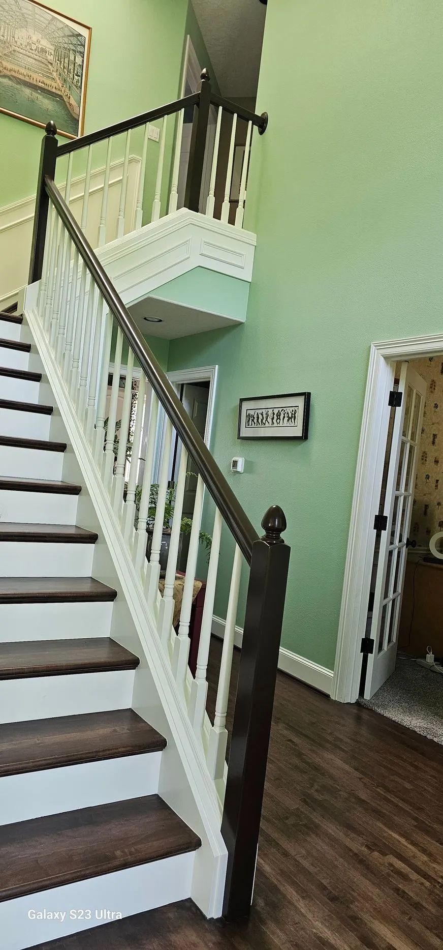 Staircase with white railing and dark wood steps in a light green hallway, with an upper landing visible.