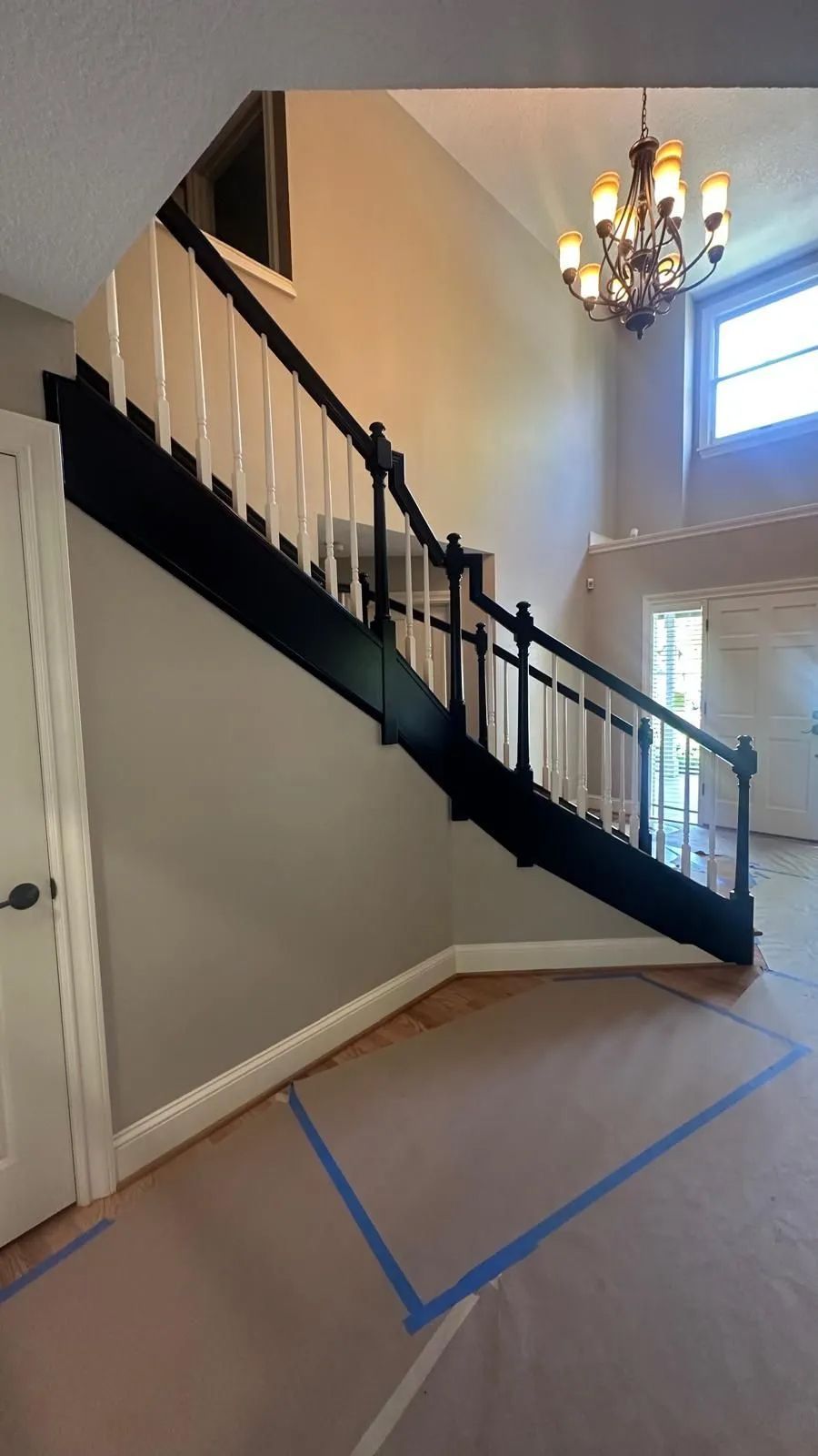 Interior staircase with black railing, chandelier, and blue tape marking a floor area.