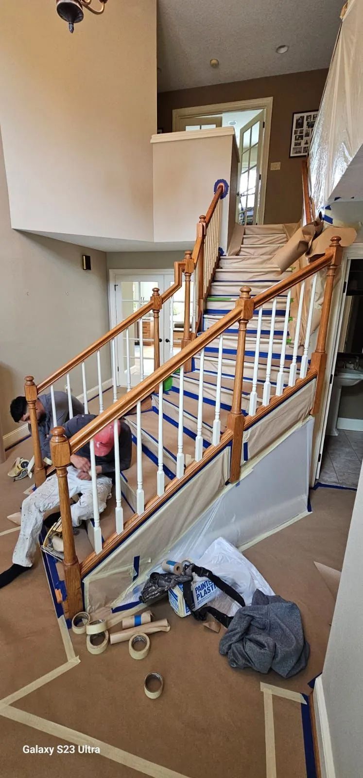 Staircase with wooden railing, drywall tools, and debris in a home under construction