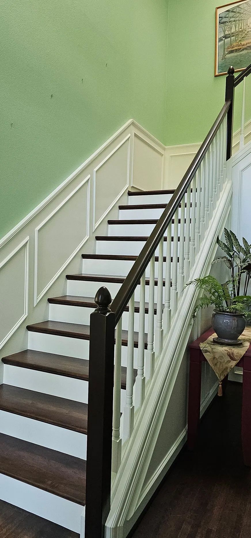 Indoor staircase with white railings, dark wooden steps, and a light green wall.