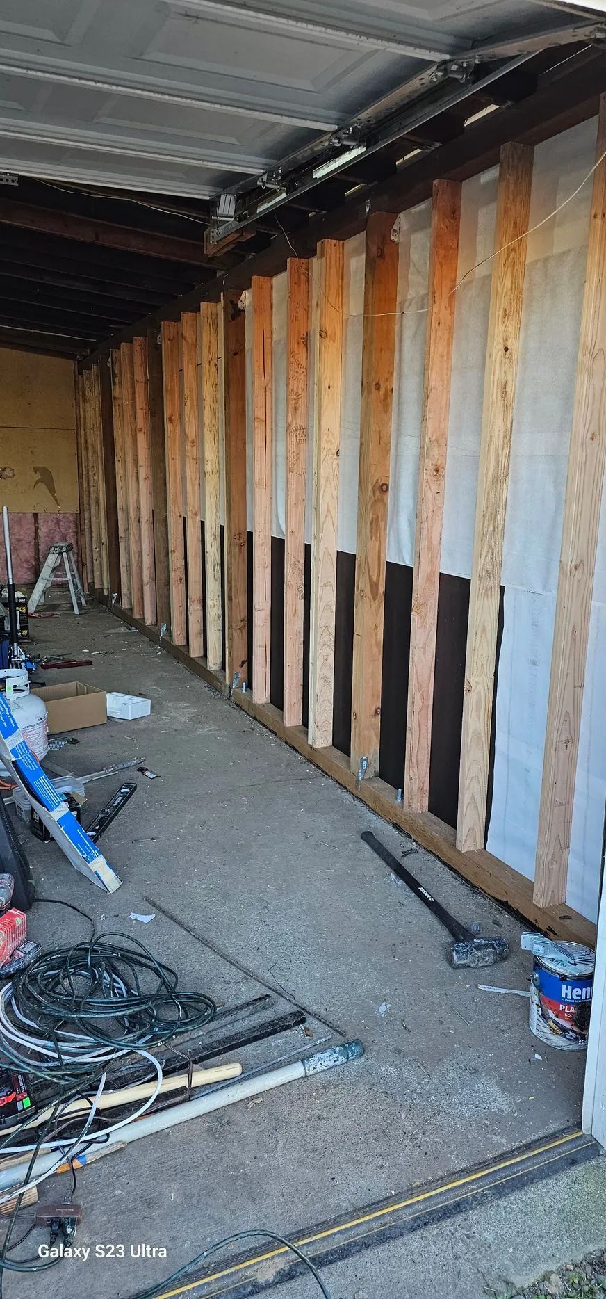 Interior construction site with exposed wall studs, insulation, and scattered tools on the floor