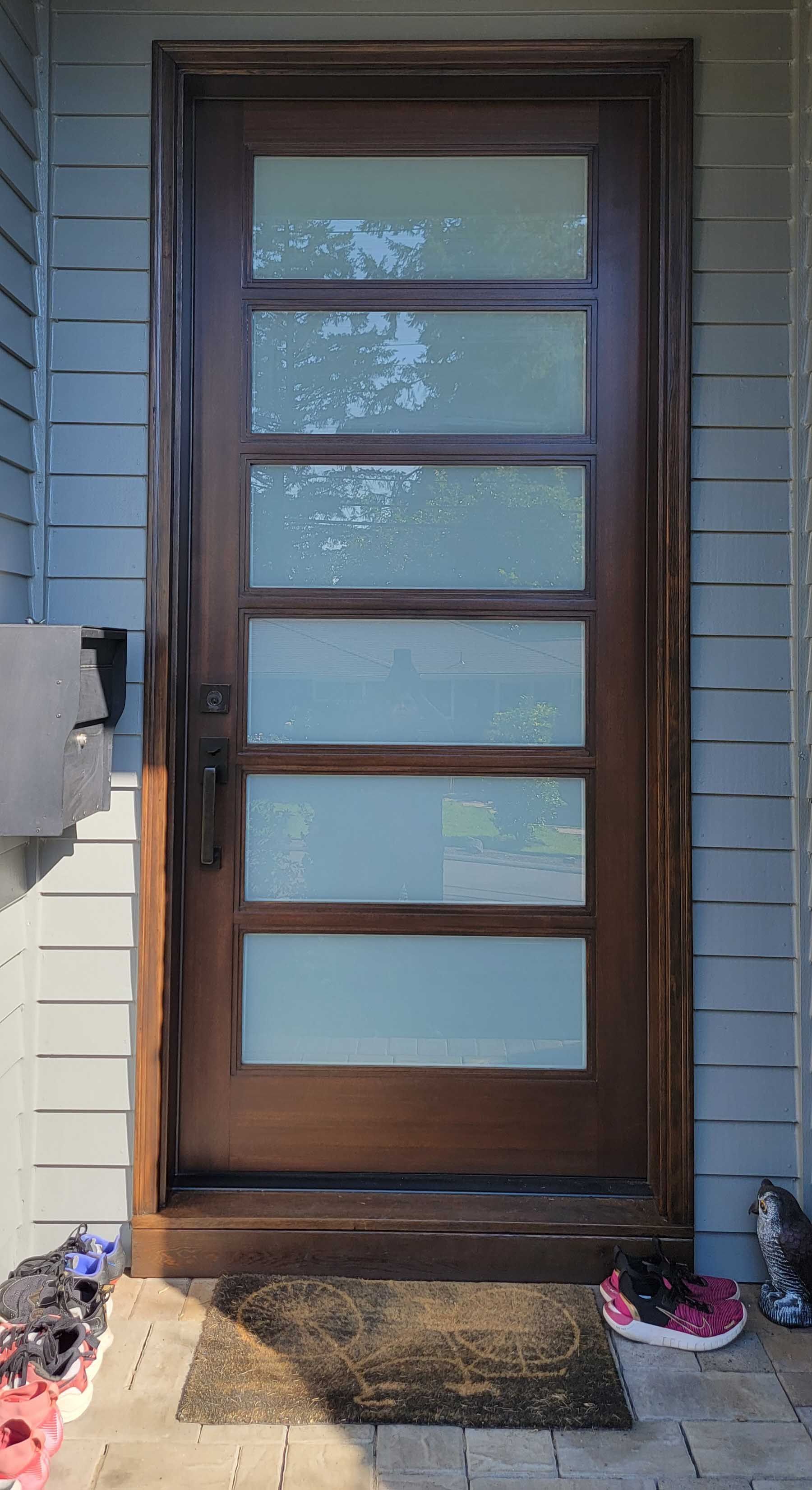 Brown front door with rectangular glass panes, set in blue siding.