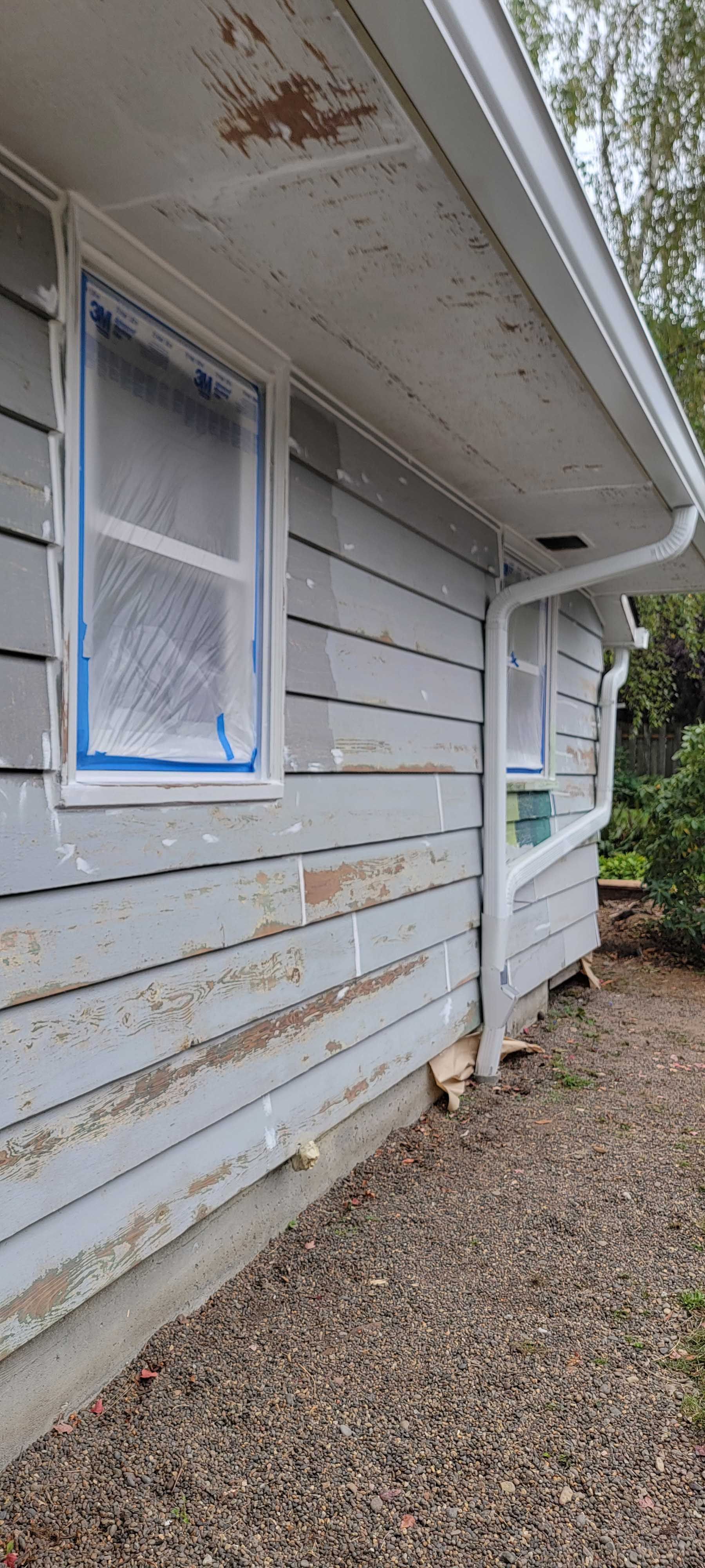 Exterior of a house with peeling paint, a white gutter, and a window covered in protective material.