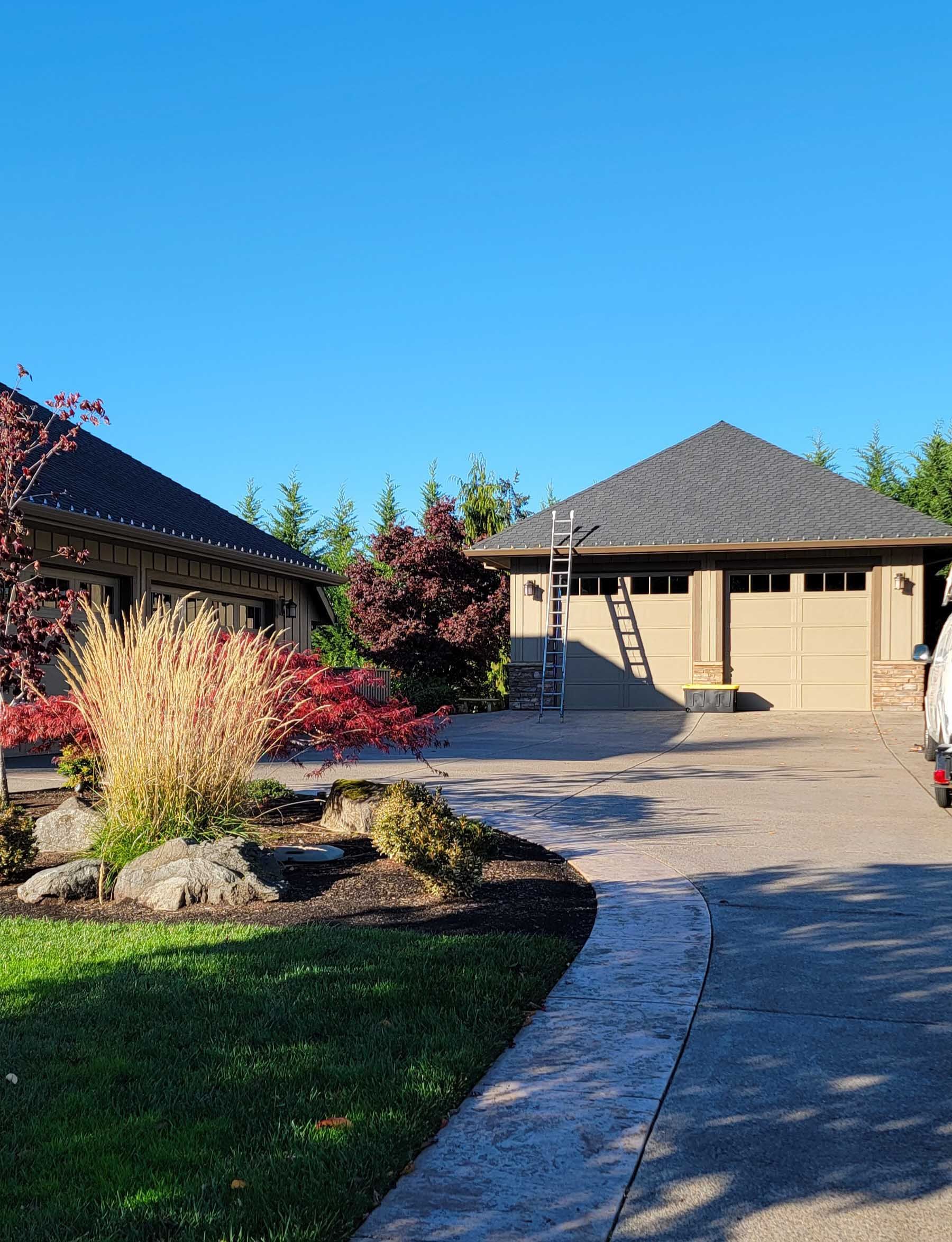 A house and garage with a driveway, landscaping, and a blue sky overhead.