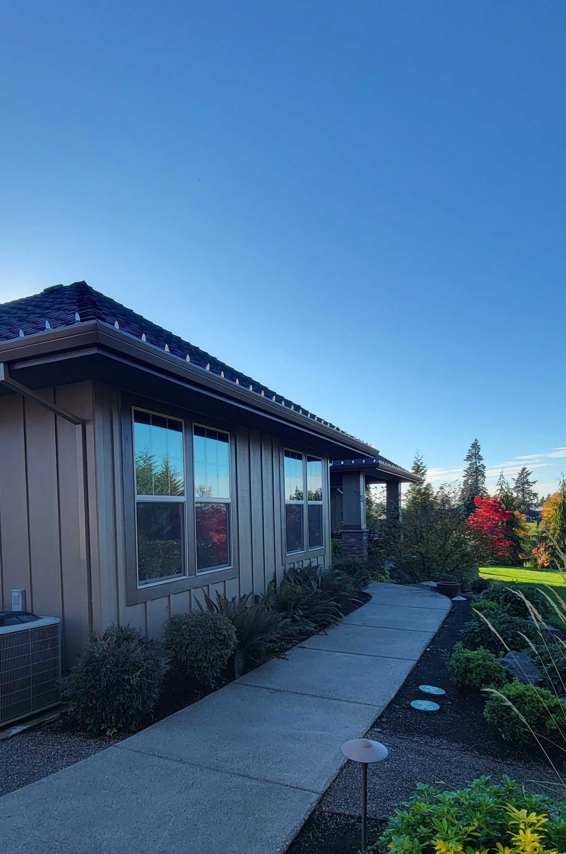 Tan house with a dark roof and a concrete walkway, under a clear blue sky.