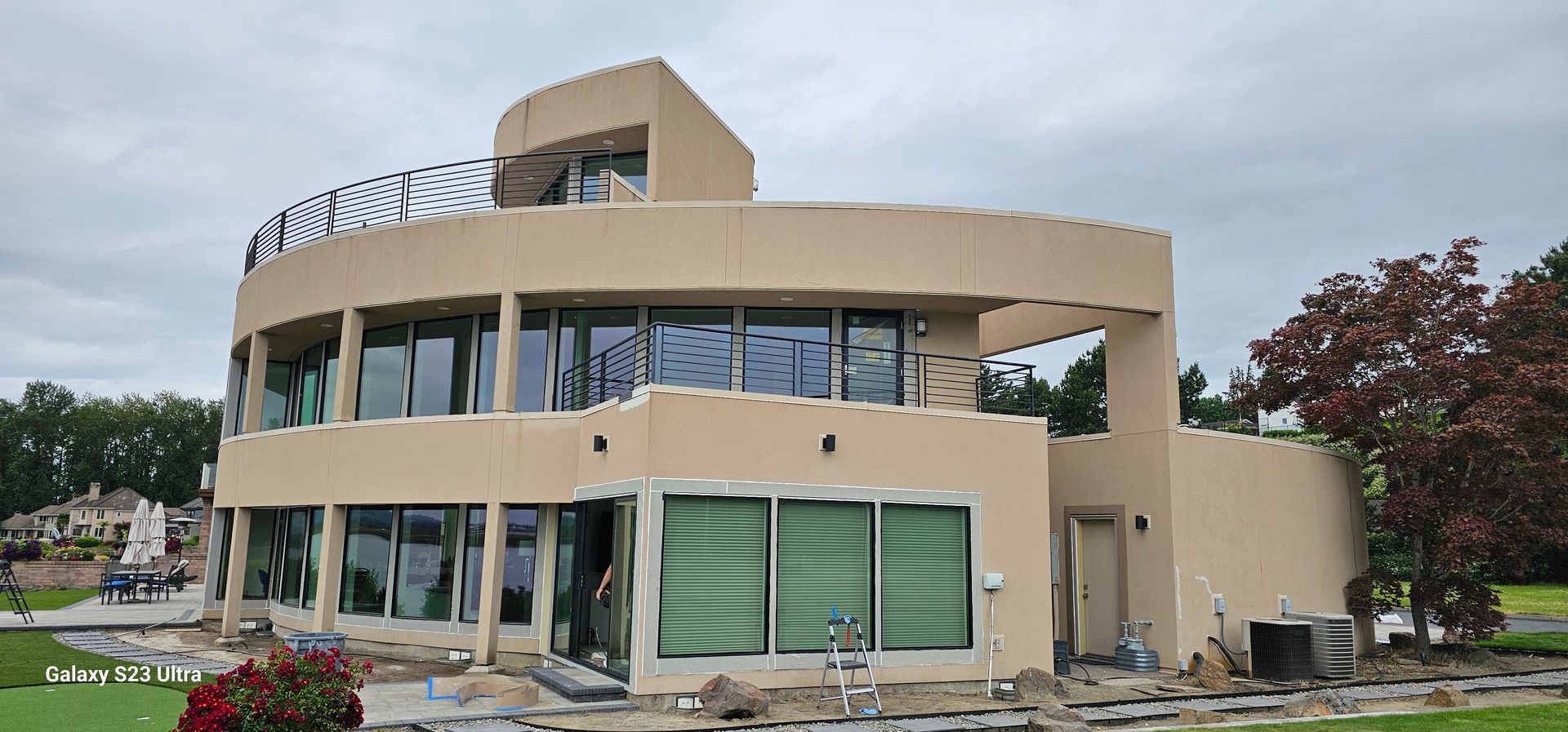 Modern, circular beige house with glass windows and a curved balcony, under a cloudy sky.