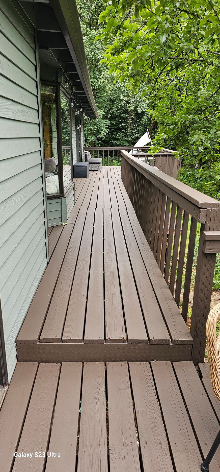 Wooden deck and railing alongside a house, surrounded by trees.