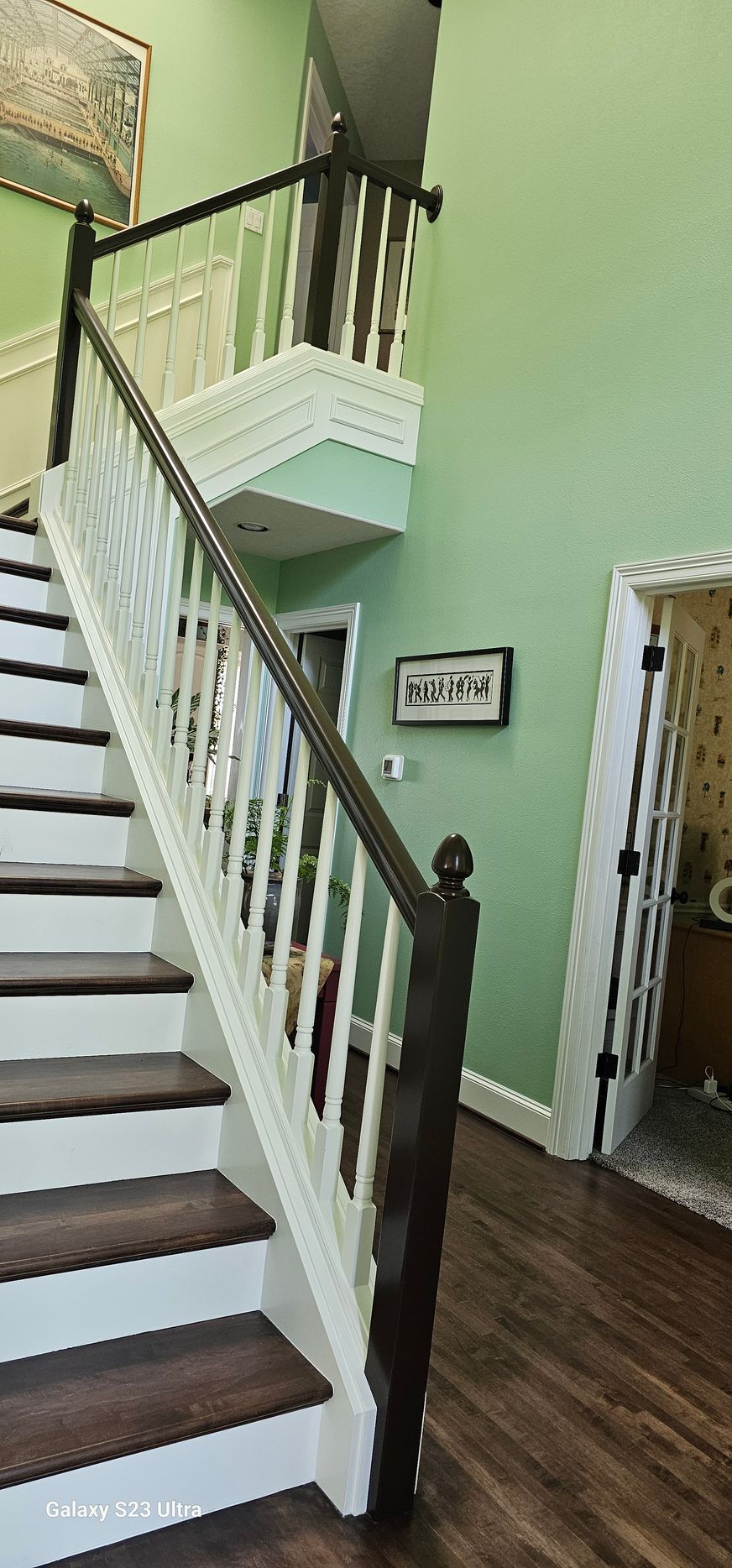 Staircase with wooden steps and white balustrade, dark brown handrail. Green walls and wood floor.